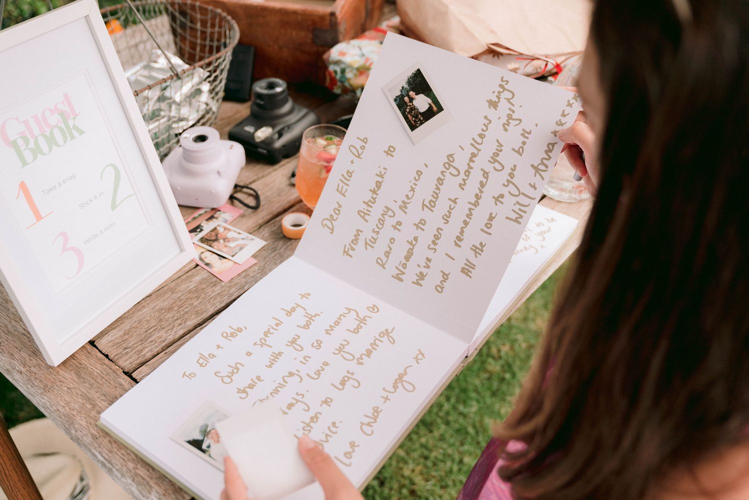 Someone writing in a guest book at a rustic wooden table with wedding decorations.