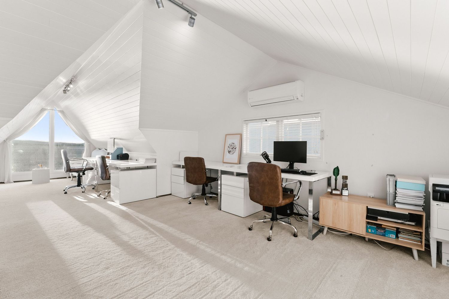 Modern white attic office space with sloped ceilings, desks and computer workstations.