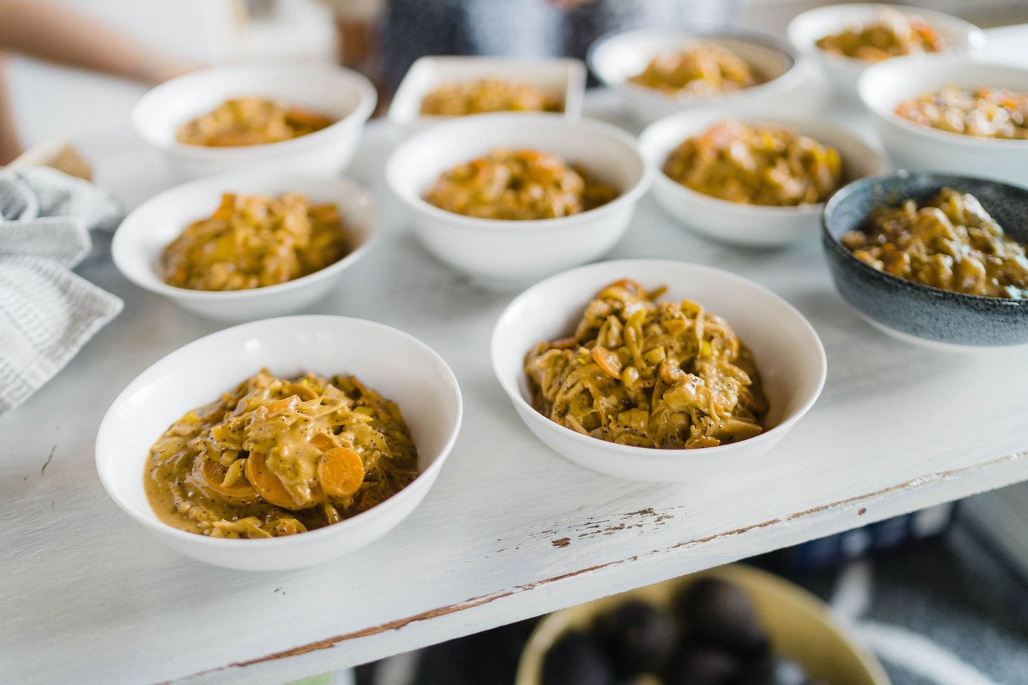 Rows of golden mac and cheese portions in white bowls arranged on a light colored surface.