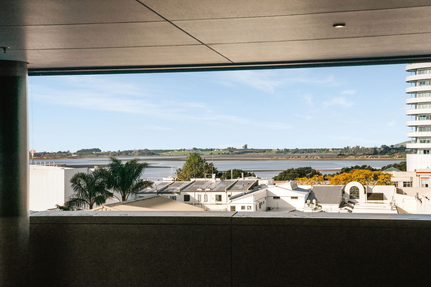 View through parking garage opening showing coastal buildings and waterfront landscape on a sunny day.