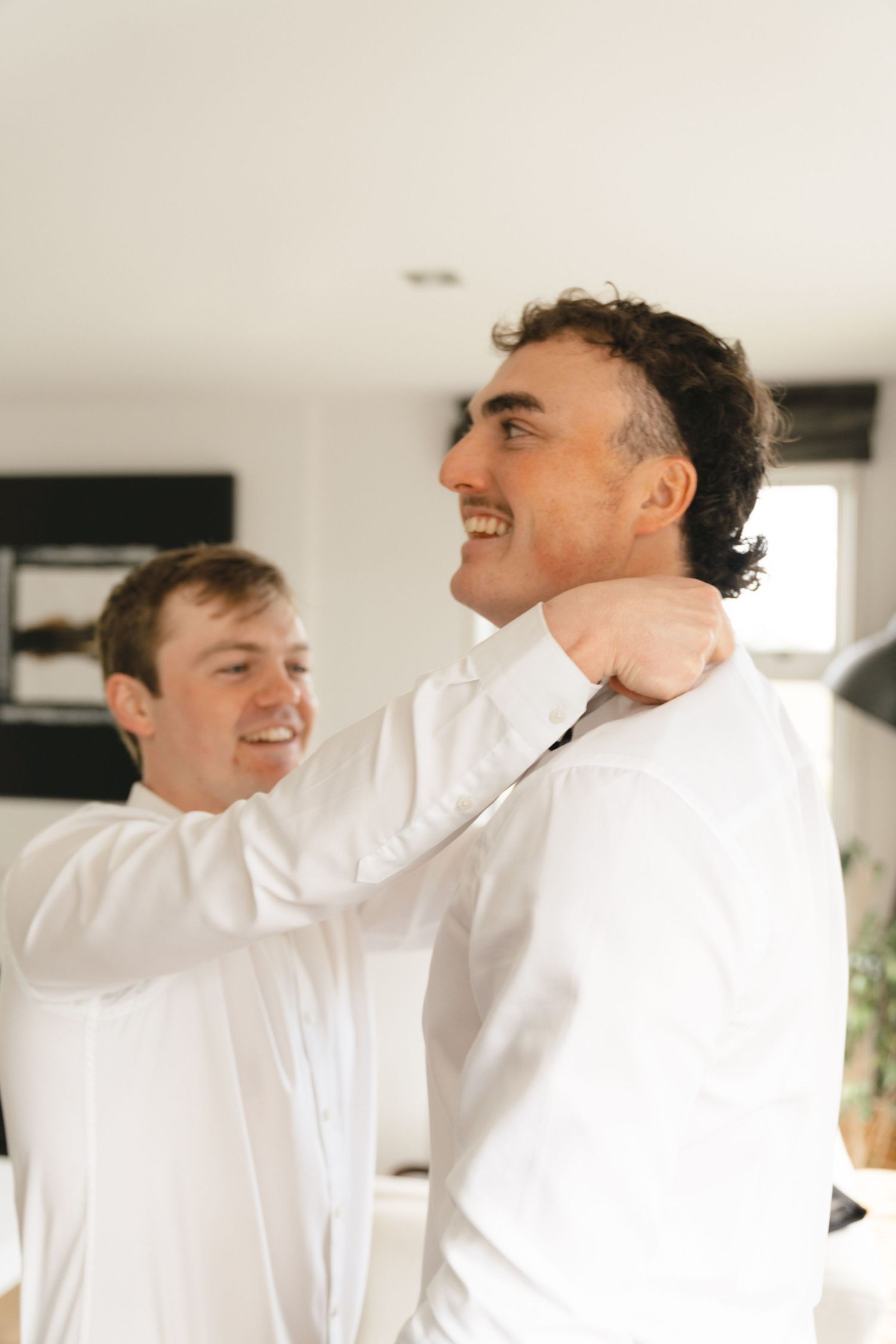 Two men in white dress shirts sharing a joyful moment indoors.