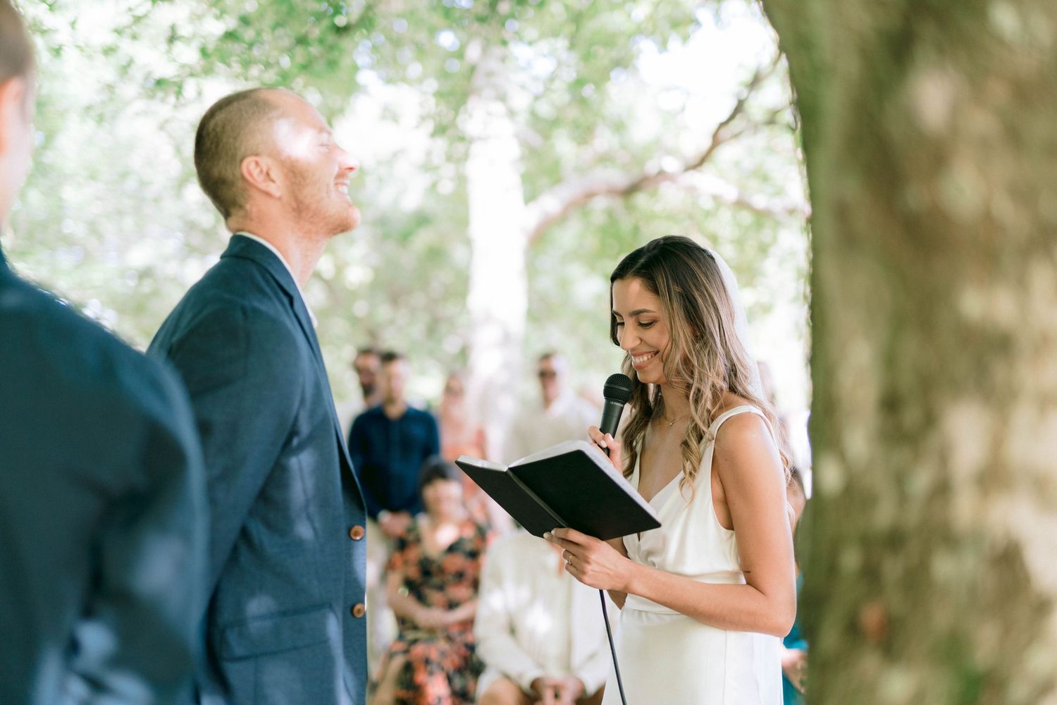 A wedding party celebrating outdoors under trees on a sunny day.