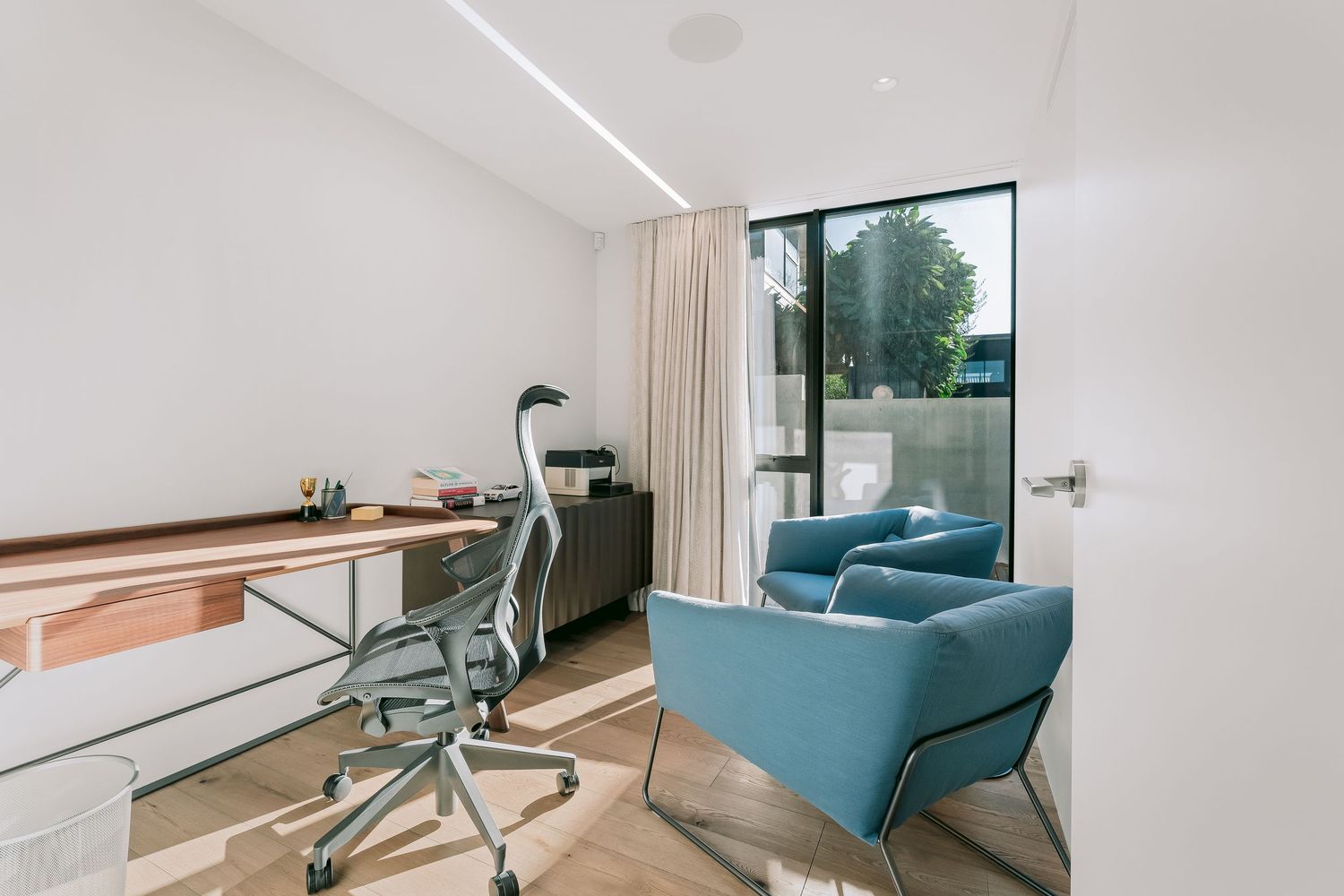 Modern minimalist living space with teal accent chair and floor-to-ceiling windows providing natural light.