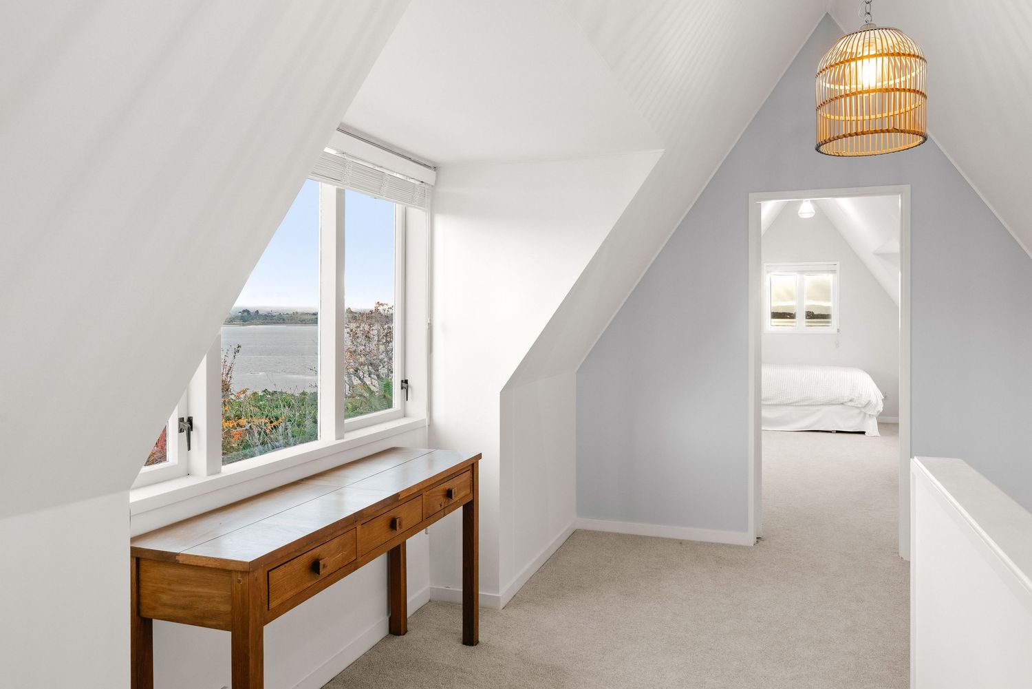 A bright attic room with a wooden desk by a window offering scenic views.