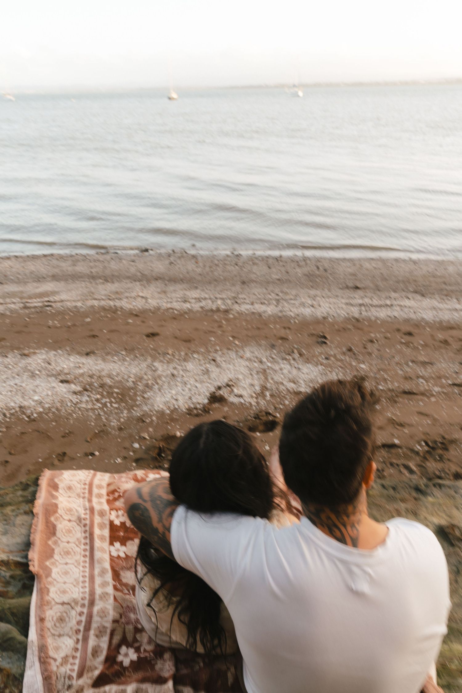 Couple sitting on a blanket at the beach during sunset enjoying a peaceful moment by the ocean.