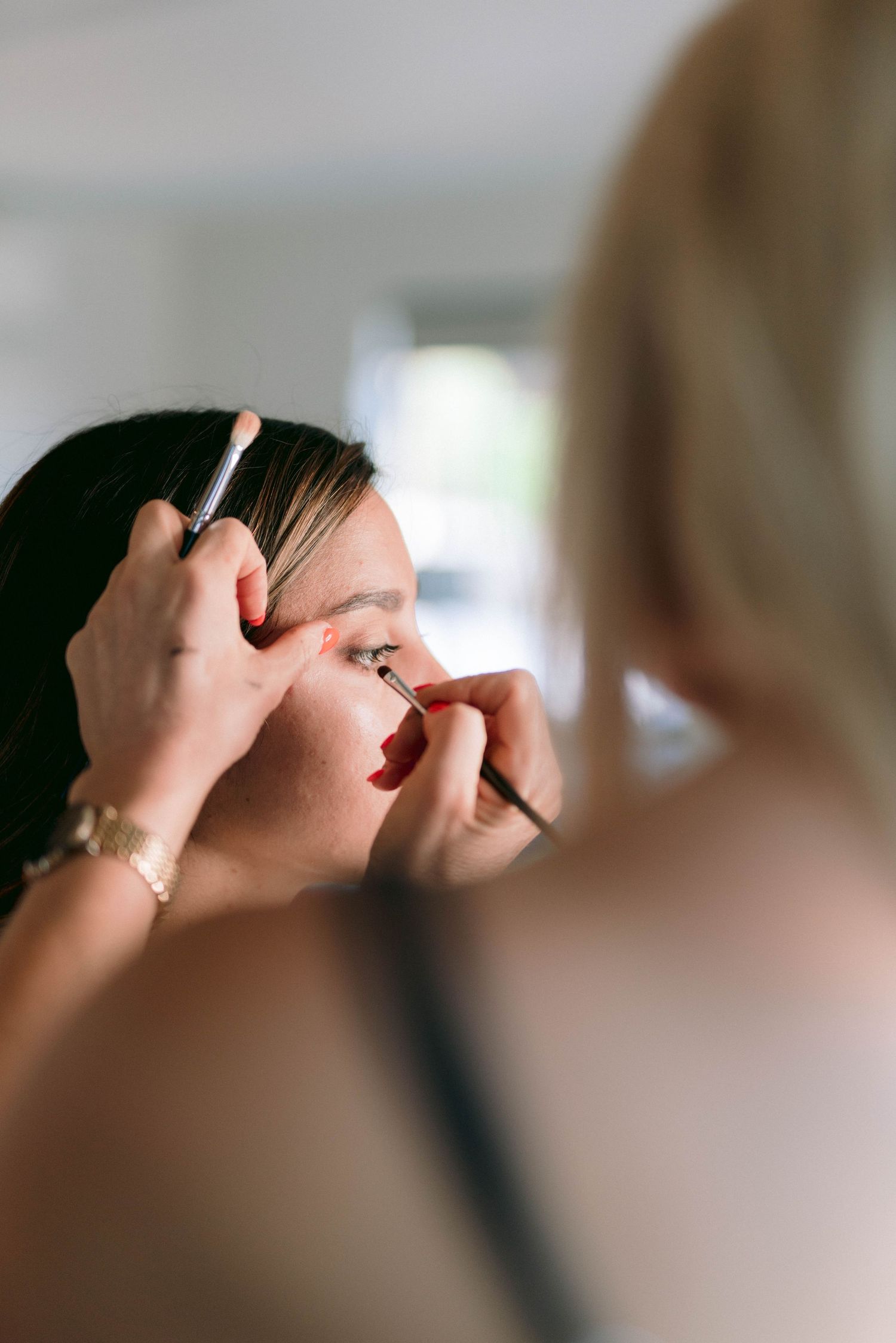 Close-up of a makeup artist applying subtle eye makeup with a small brush in soft natural lighting.