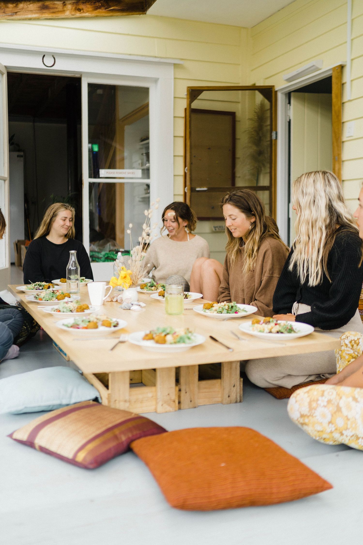 Friends enjoying outdoor brunch gathering on porch with cushions and shared plates.