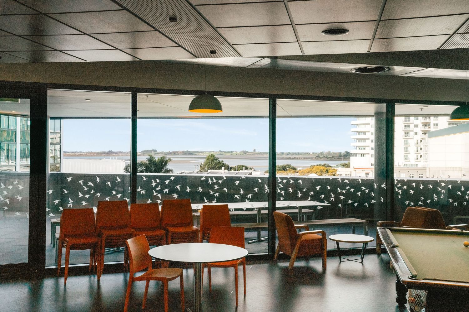 Modern lounge area with retro orange chairs overlooking a scenic view through large windows with decorative decal patterns.