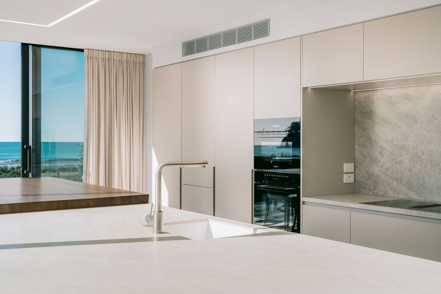 Minimalist white kitchen with ocean views and modern appliances built into sleek cabinetry.