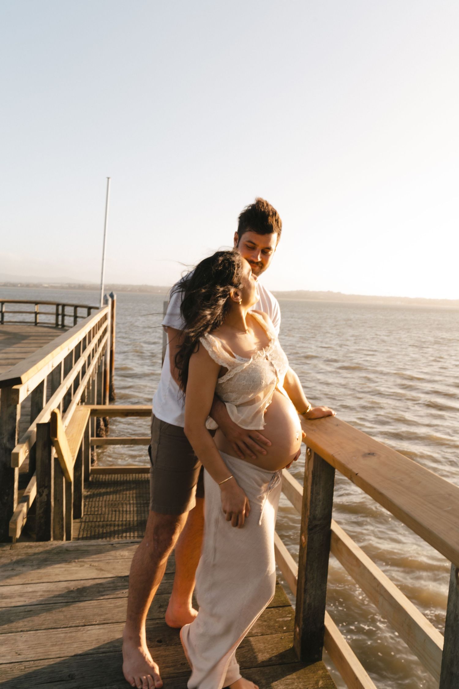 A couple shares a romantic moment on a wooden pier at sunset overlooking the water.