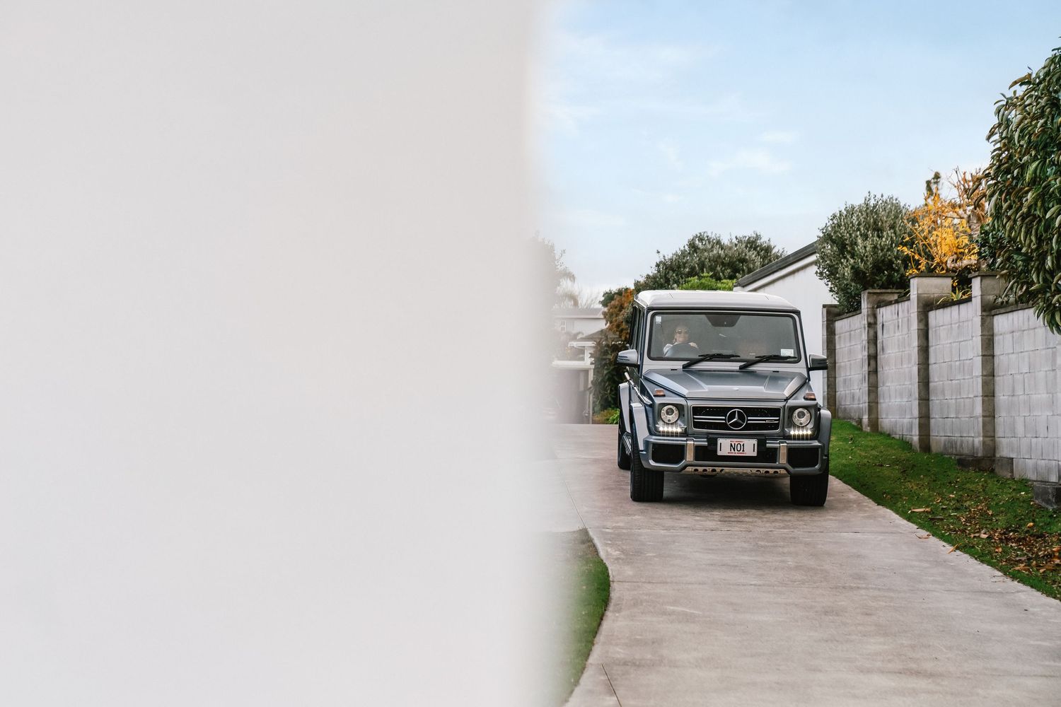 A black Mercedes-Benz G-Class SUV parked on a concrete driveway beside a white wall.