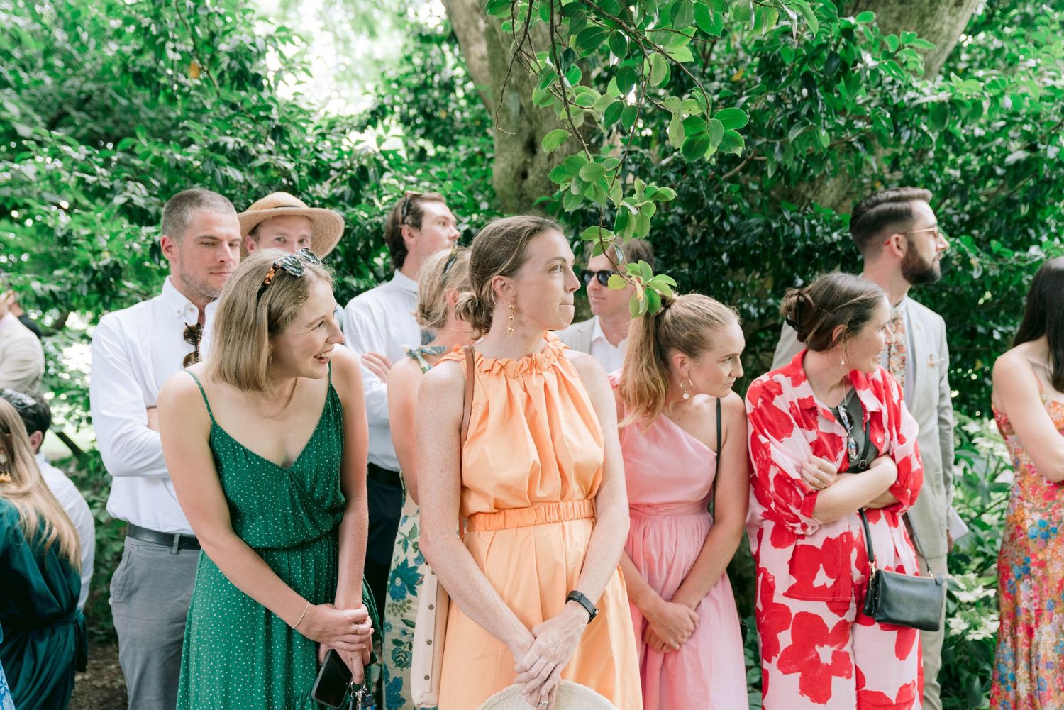Wedding guests in colorful summer dresses gathered outdoors.