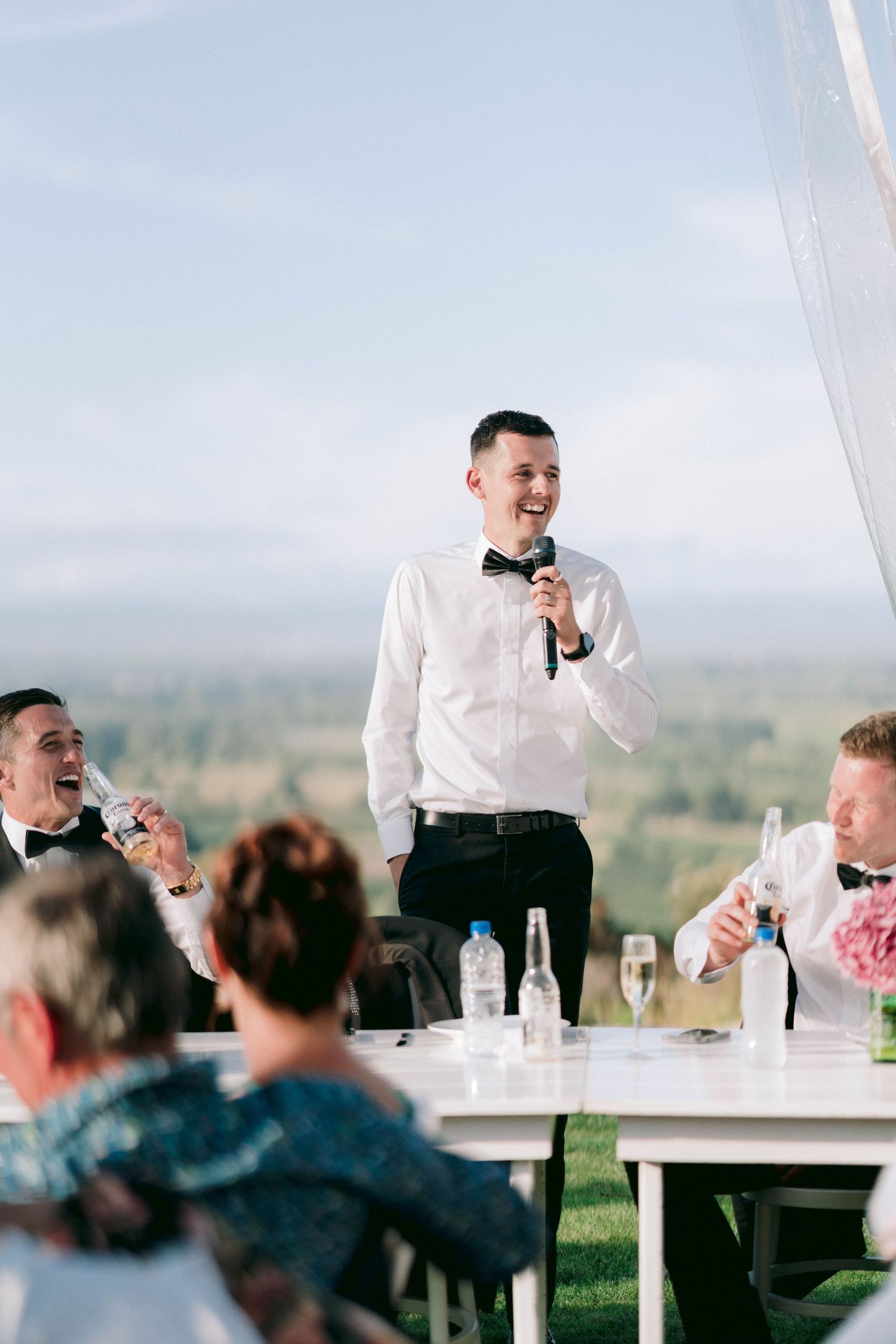 A guest gives a speech during an outdoor wedding reception under a white tent.