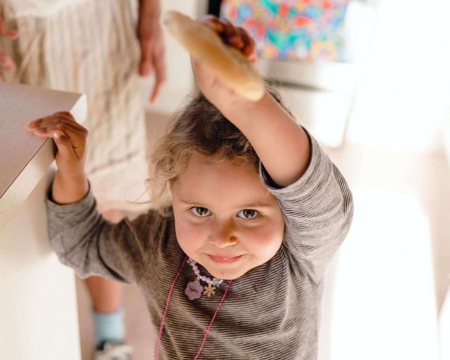 A child in a grey sweater reaching up playfully in bright indoor lighting.