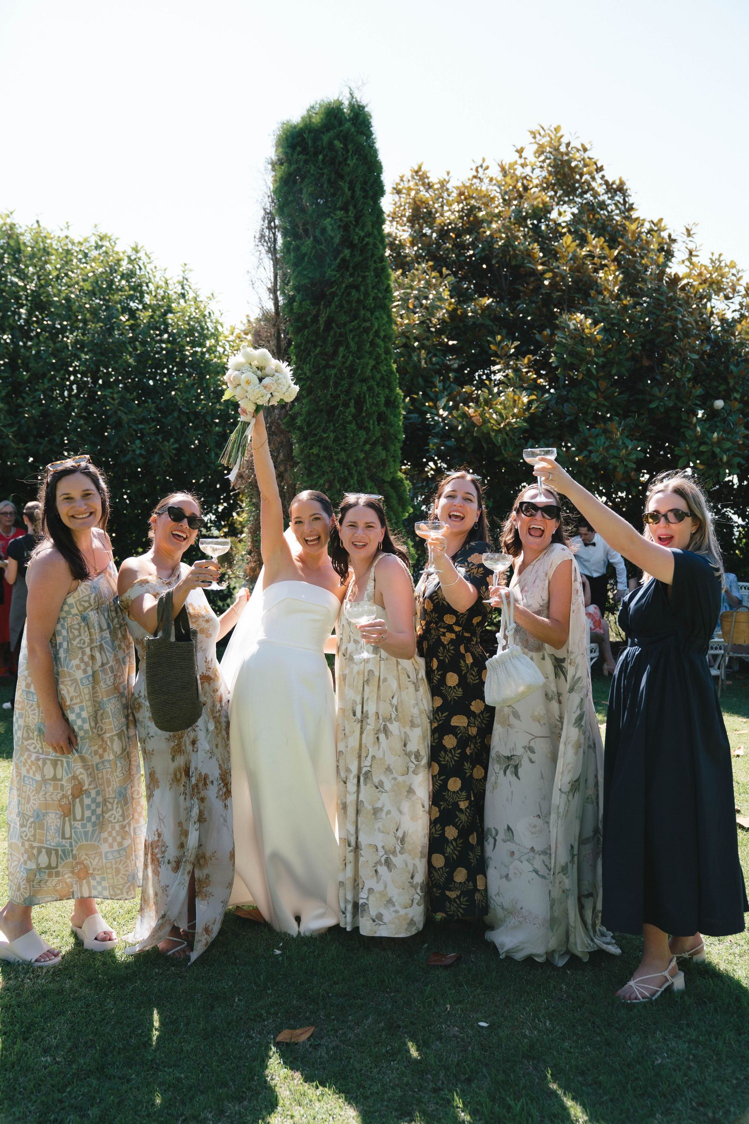 Wedding party in floral print dresses poses outdoors in a garden setting.