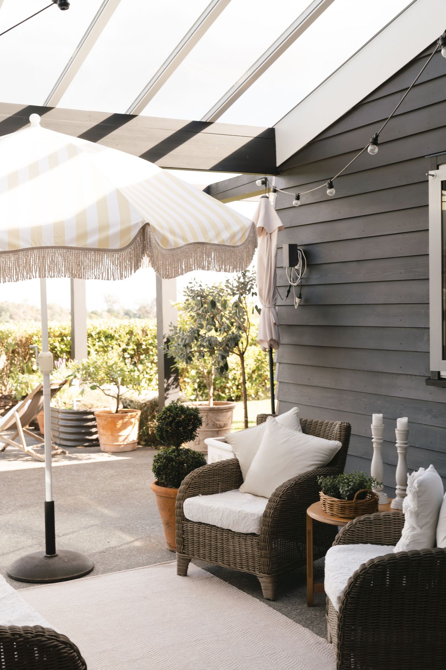 Elegant covered patio with wicker furniture, white cushions, and striped awning creates a cozy outdoor living space.