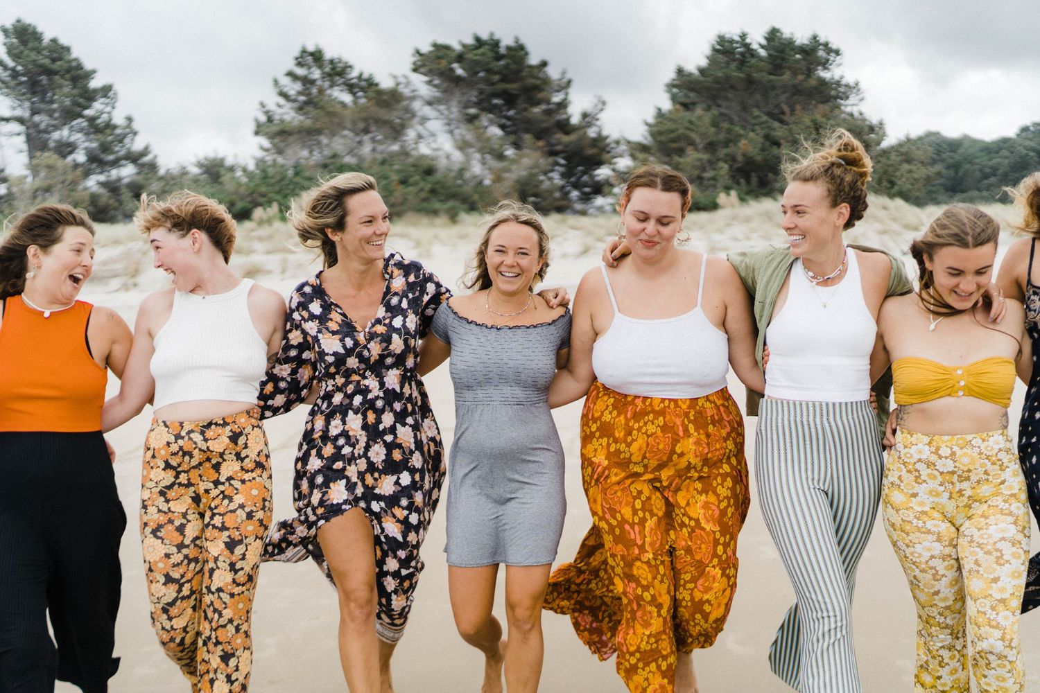A joyful group wearing colorful casual outfits walking together and laughing on a beach.