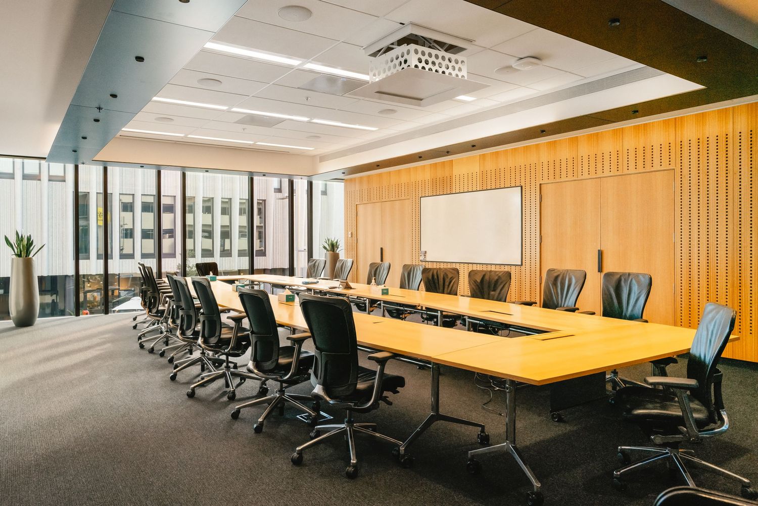 Modern corporate conference room with glass walls, wooden accents, ergonomic chairs and expansive natural lighting.