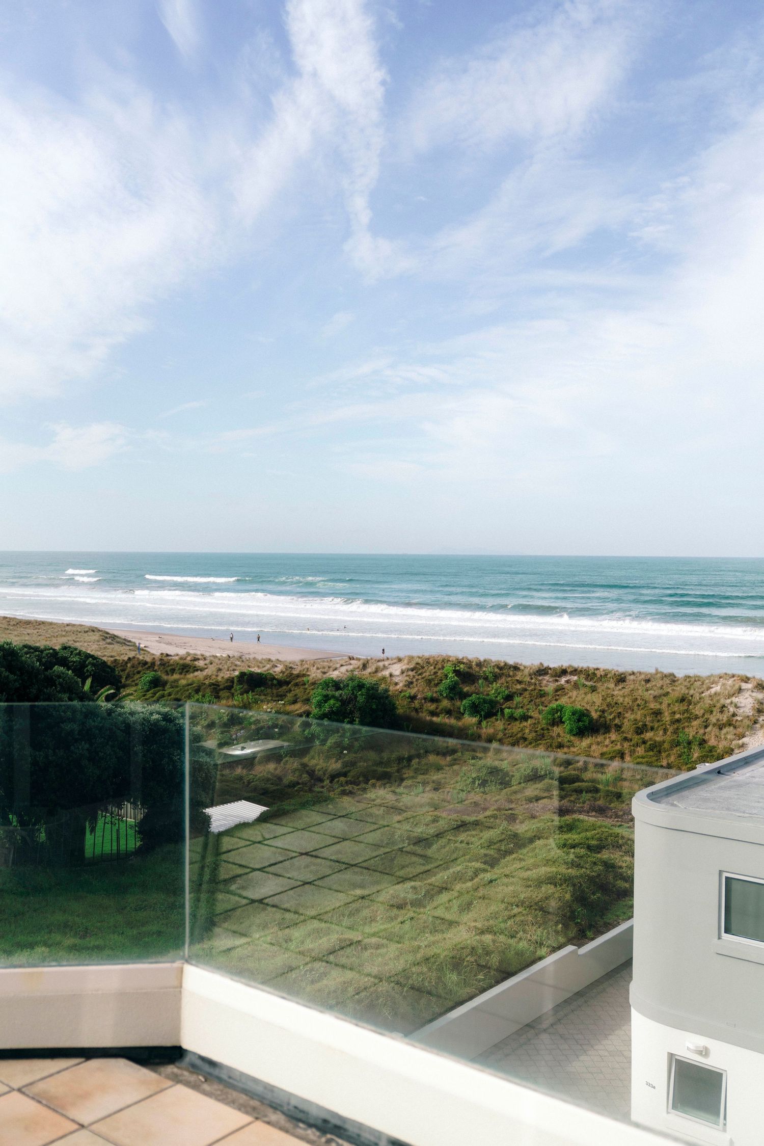 Ocean view from a modern balcony with glass railings and blue skies above.