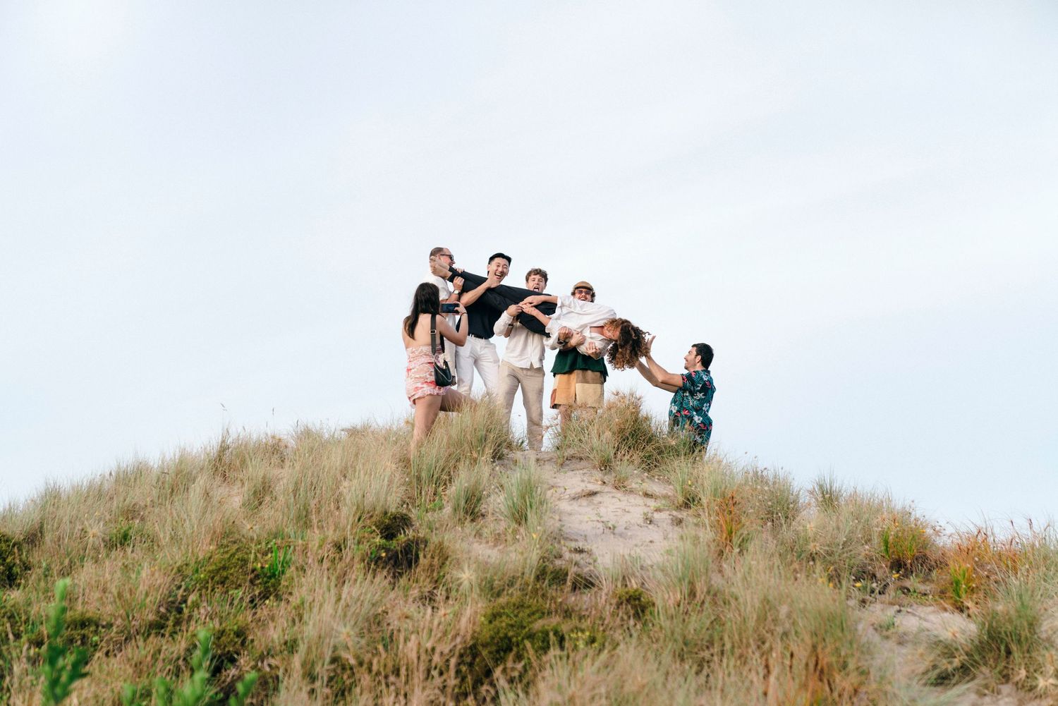 Party guests gather for a photo on a scenic hilltop against a bright sky.