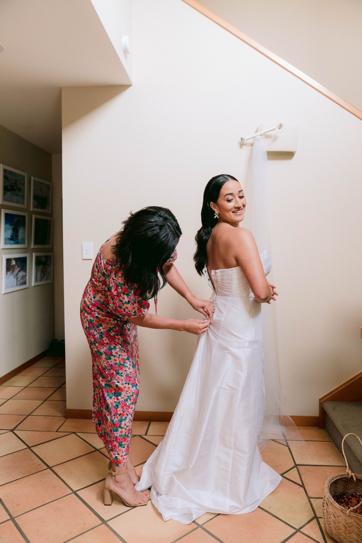 Sequence of helping the bride get dressed in white wedding gown with floral dress assistant in interior hallway.
