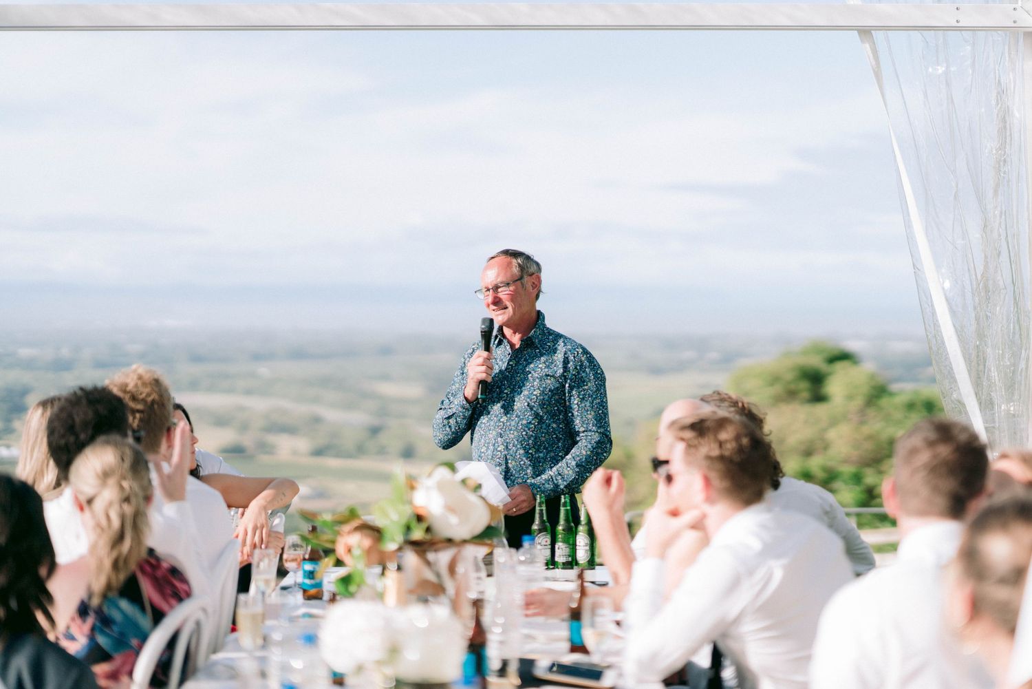 Wedding guest gives a speech during outdoor reception with scenic views.