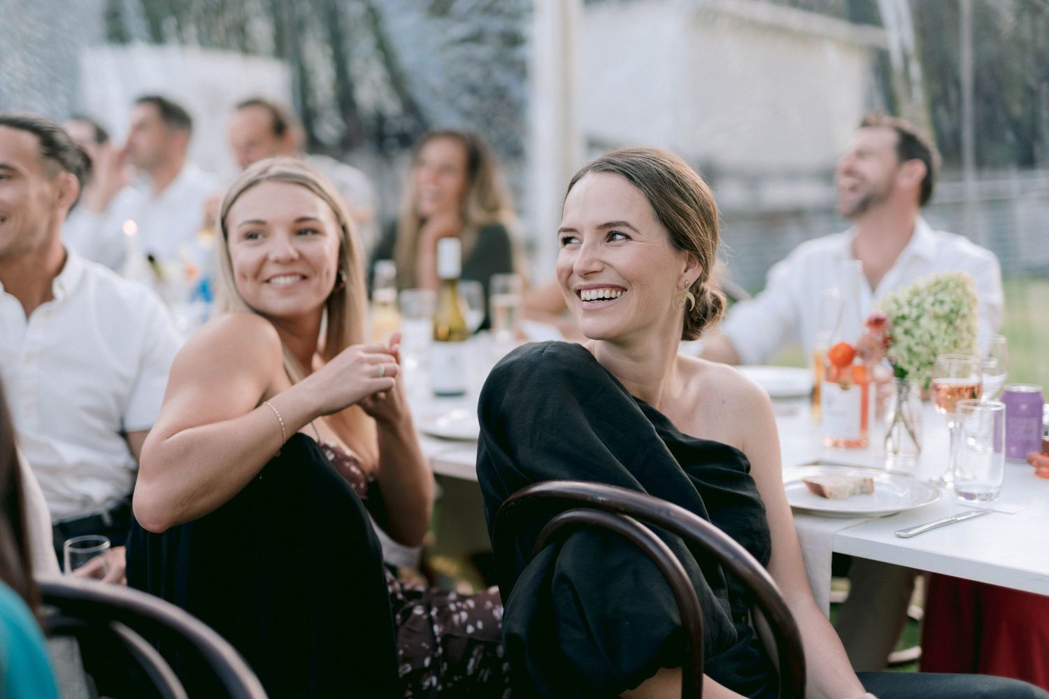 Wedding guests enjoy an outdoor reception dinner while laughing together.