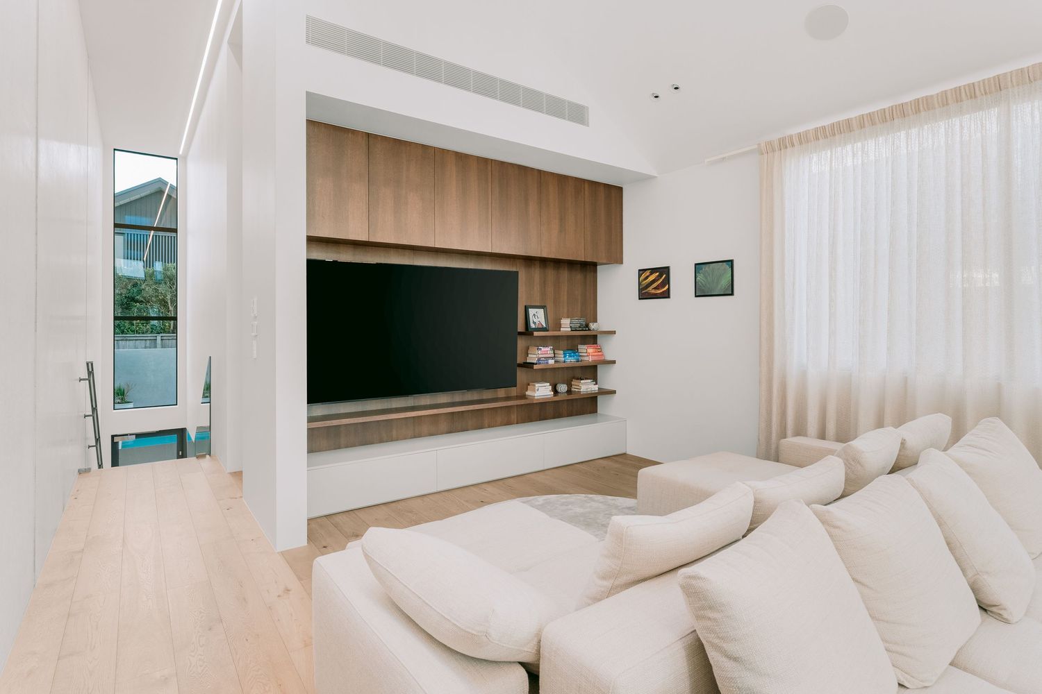 Modern living space with white sectional couch and built-in entertainment center with wood paneling.