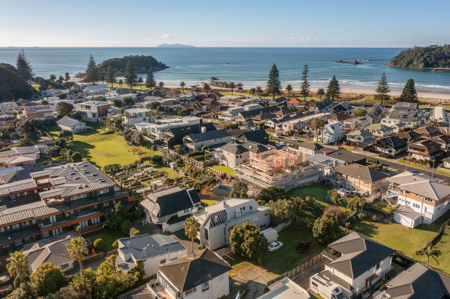 Aerial panorama of a coastal town with houses nestled along the shoreline and dramatic ocean cliffs.