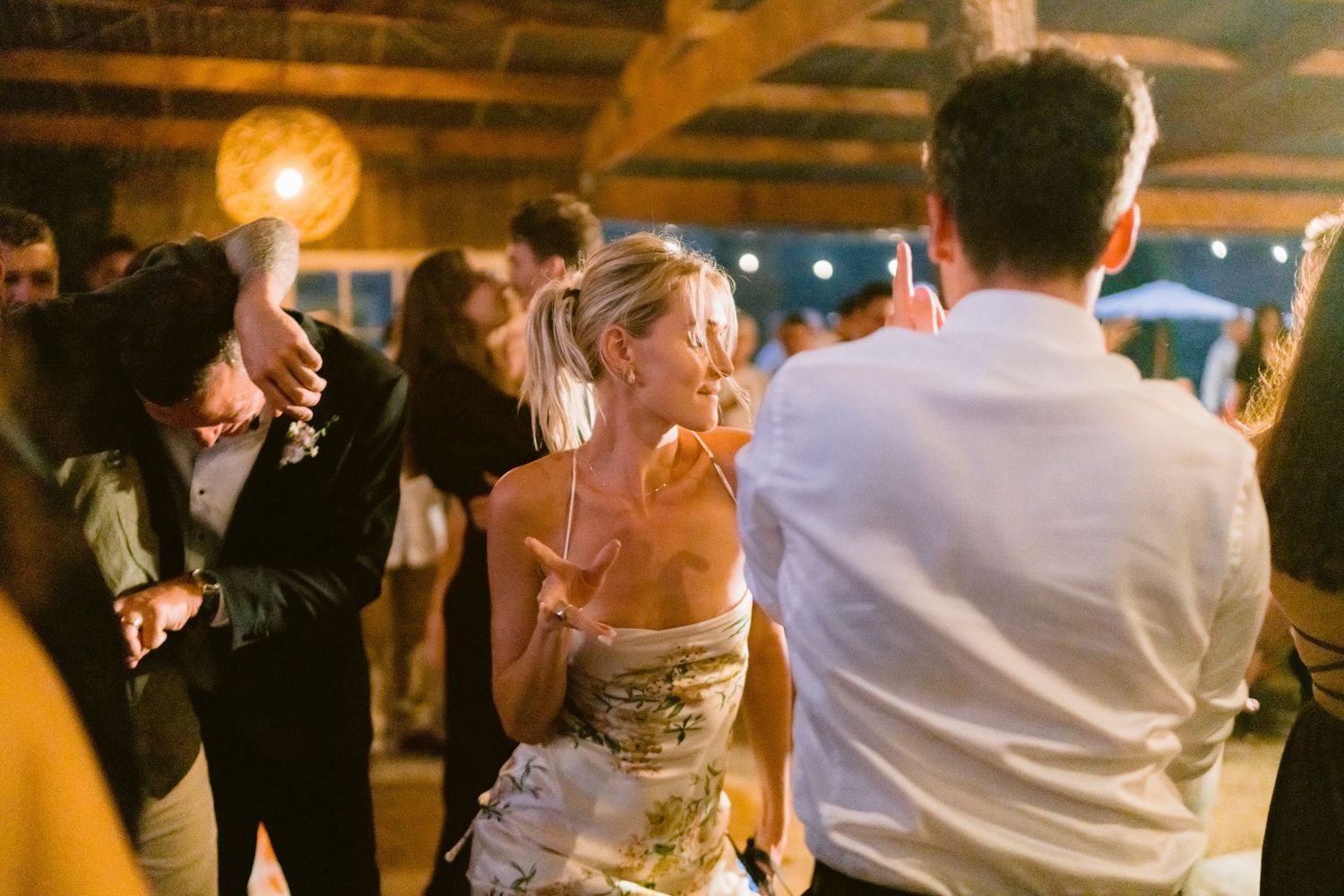 Wedding guests dancing and celebrating at an evening reception with warm lighting.