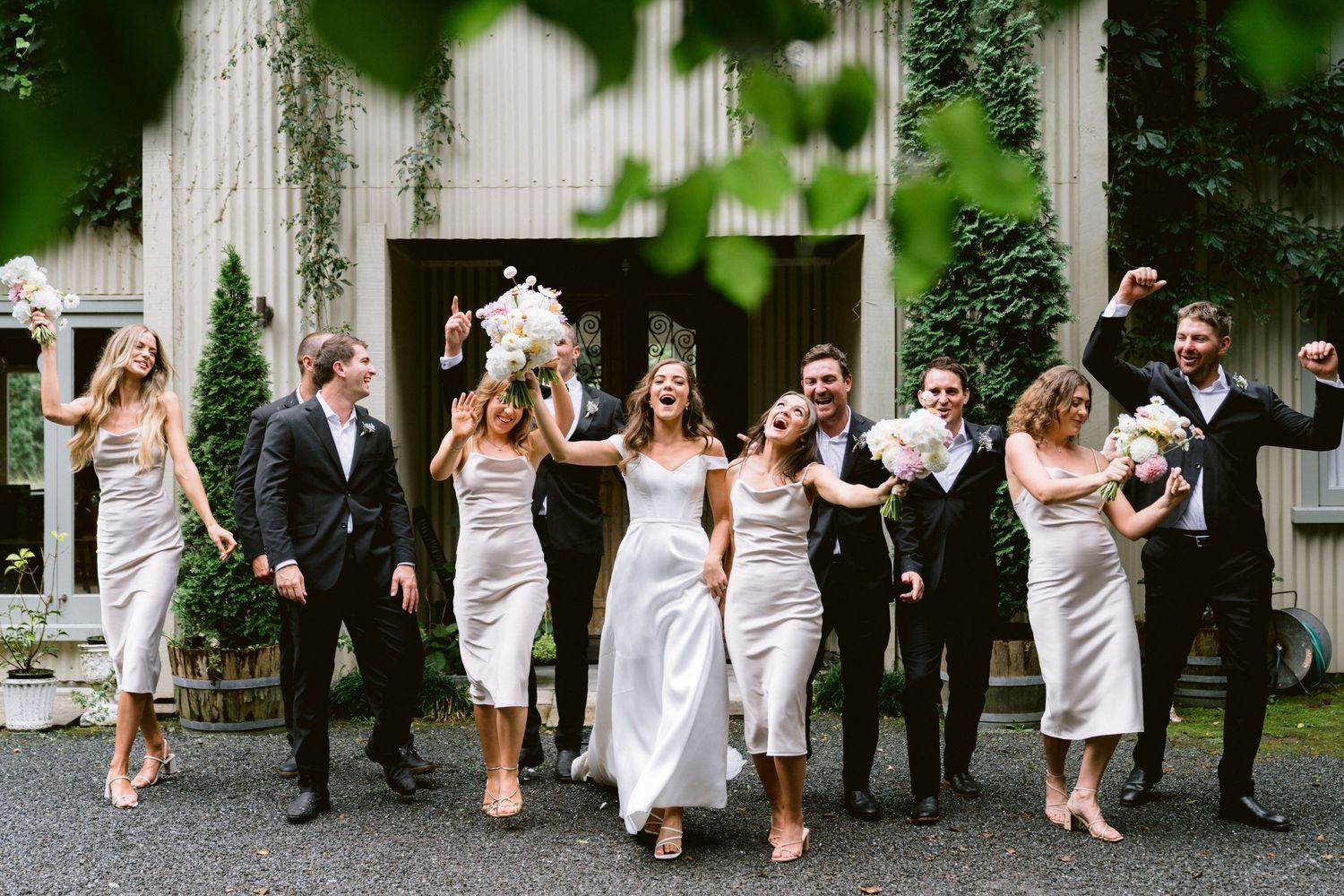 Wedding party walking and posing together outdoors with greenery in the background.