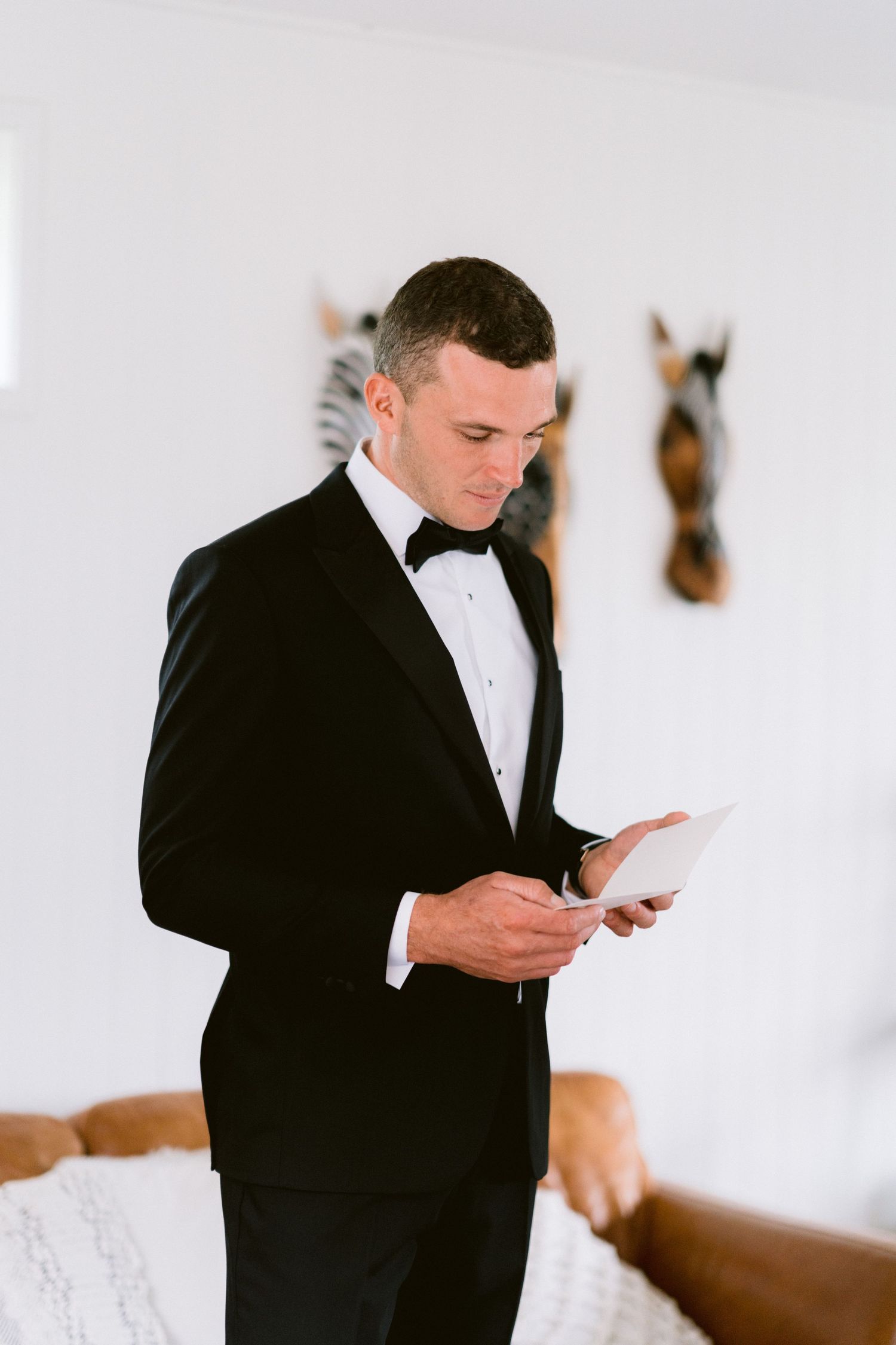 A person in a black tuxedo reads from a paper during a formal occasion.