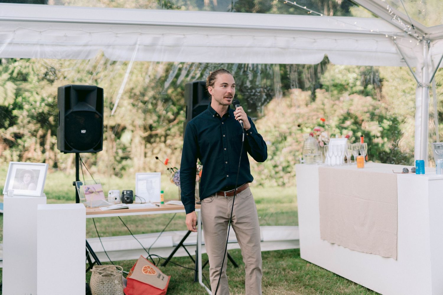 Speaker giving a speech under an outdoor tent at a wedding reception.