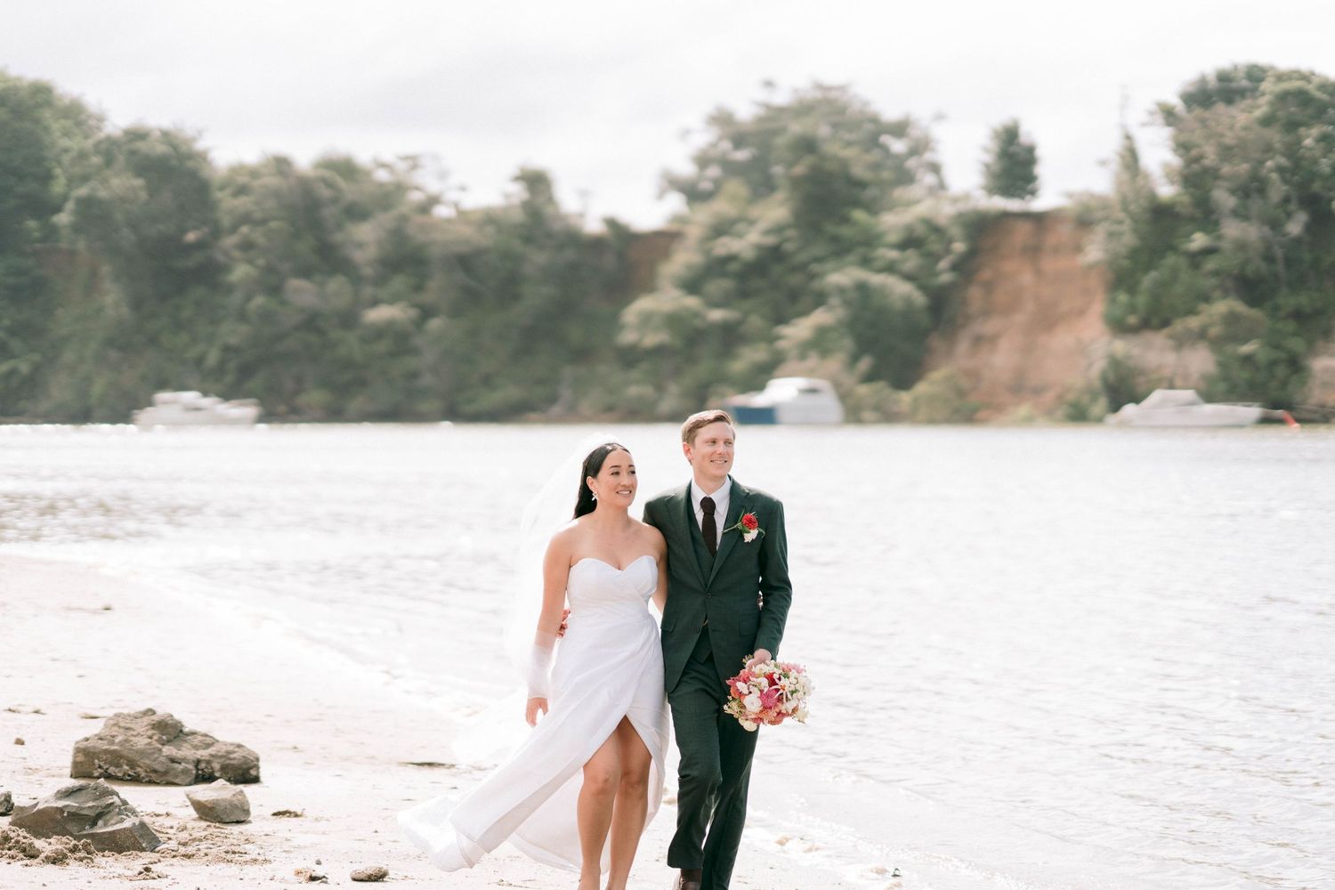 Newlyweds walking along a scenic waterfront beach.
