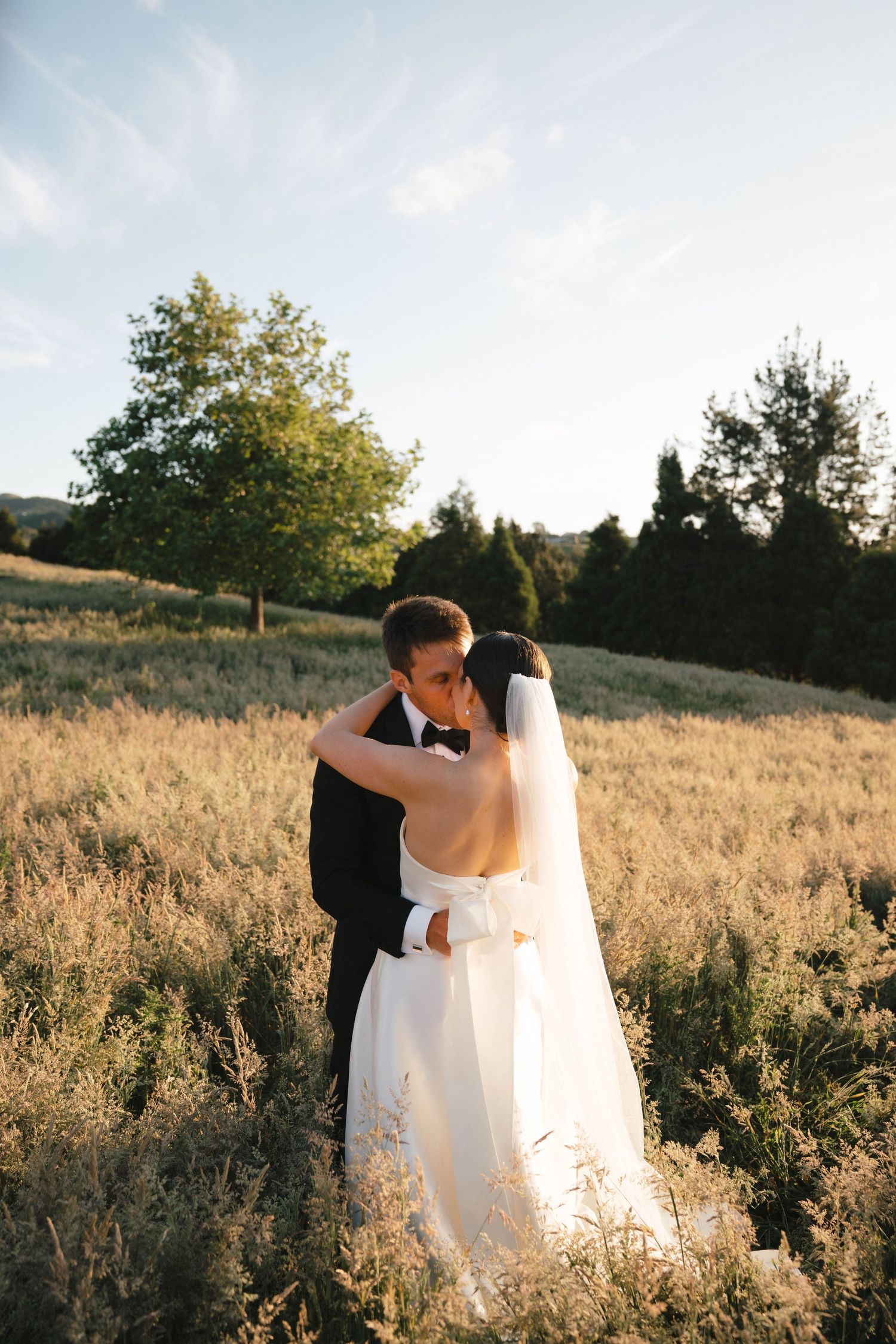 Couple in wedding attire dancing in a golden sunlit field.