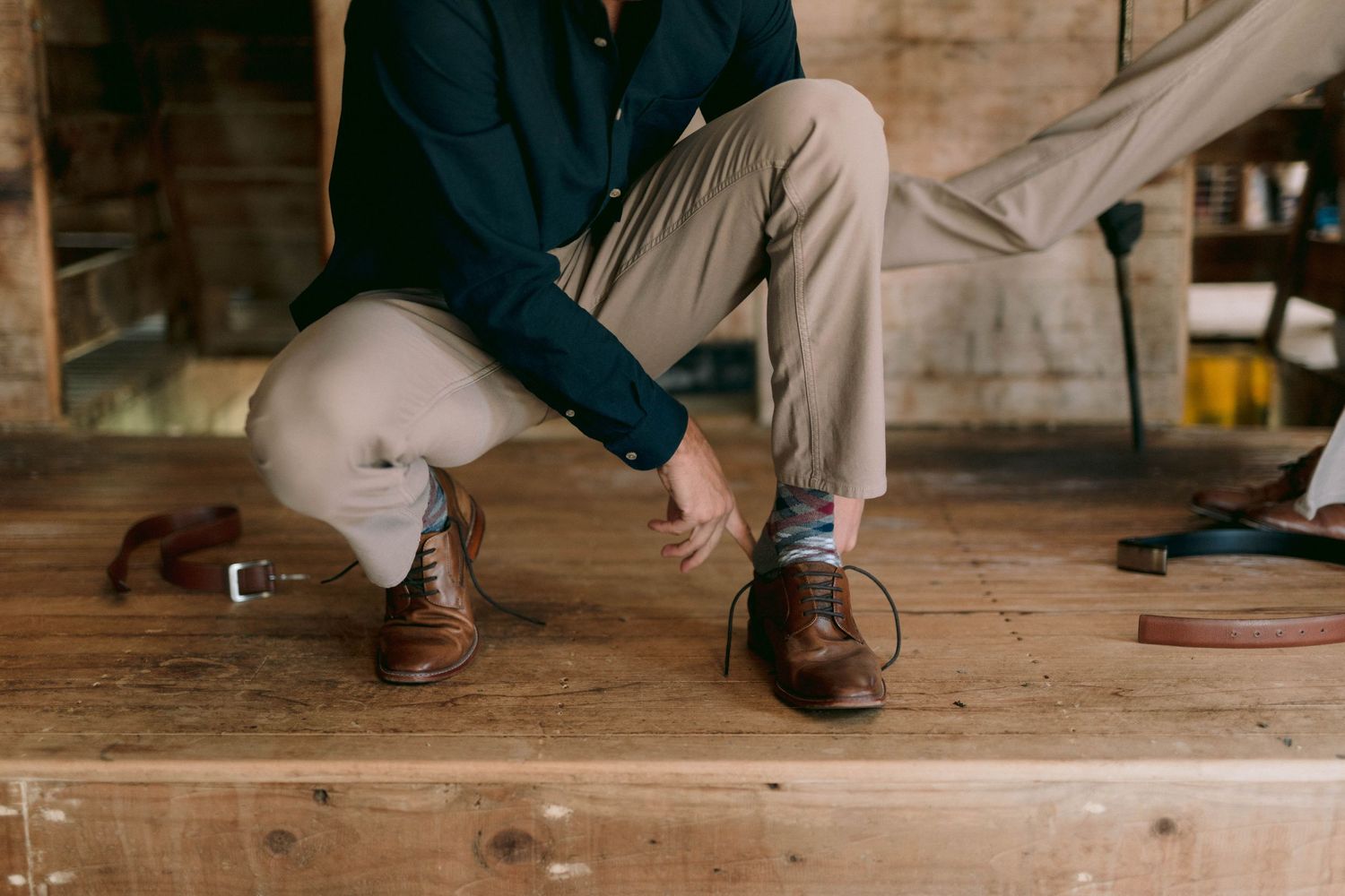 Close-up of brown leather dress shoes being tied on wooden steps.