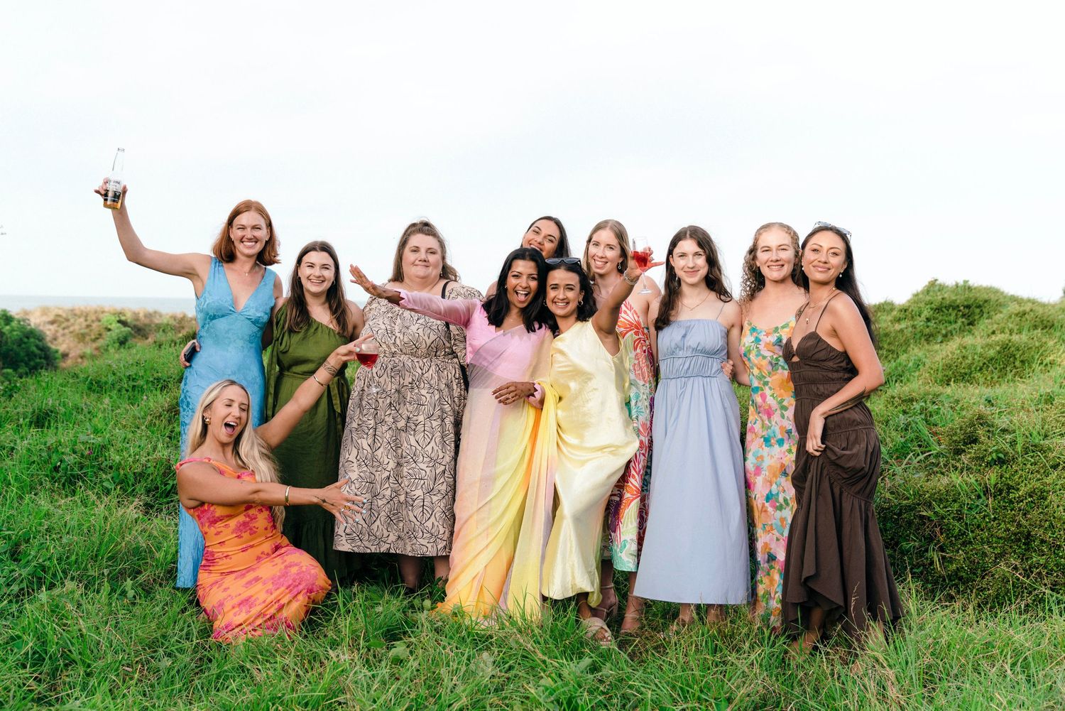 Group posing in colorful dresses against natural outdoor backdrop.