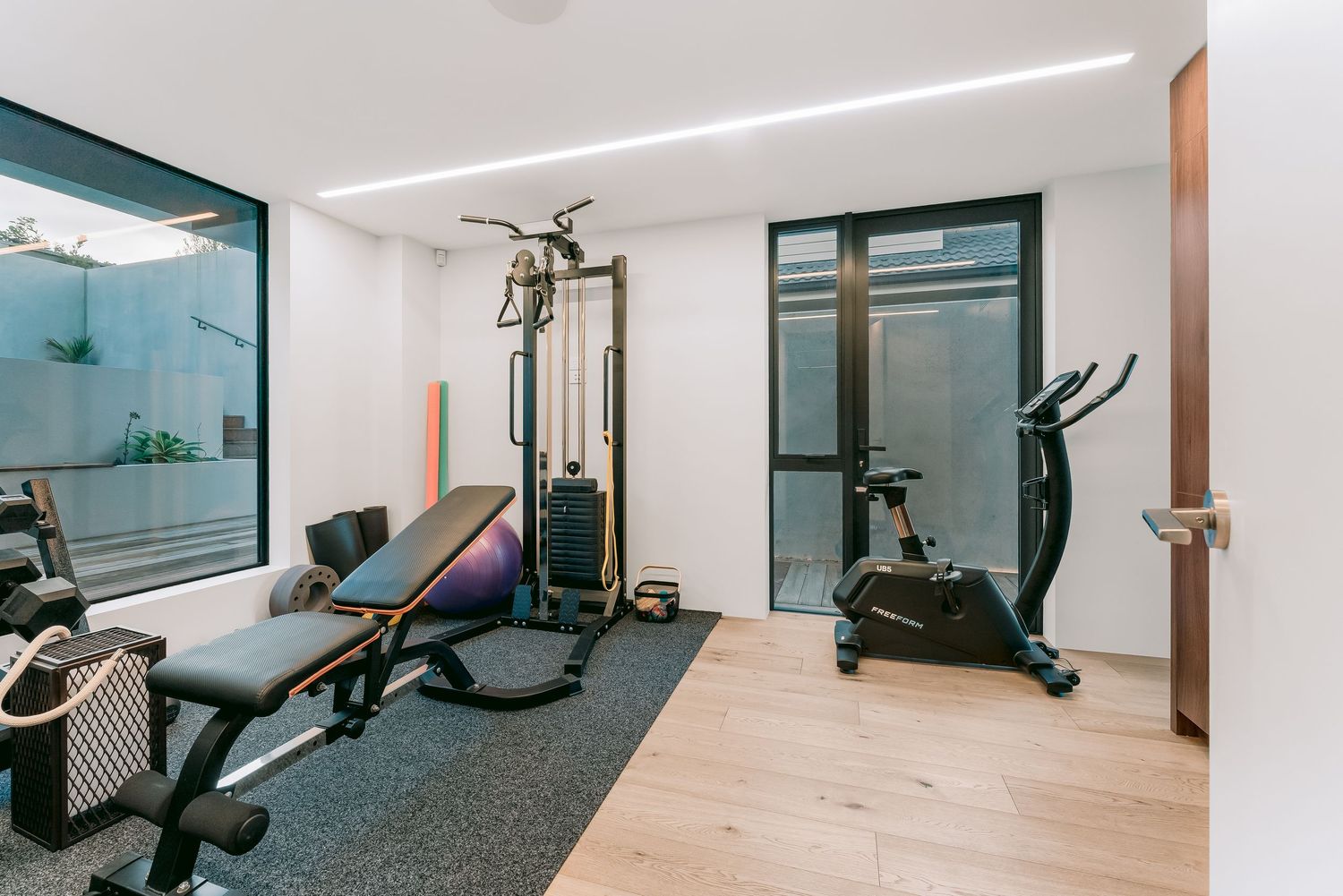 Modern gym facility with exercise equipment and bright linear lighting in clean white interior space.