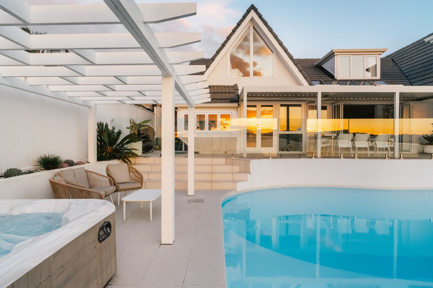 Luxury poolside setting with hot tub and covered patio area at sunset featuring modern coastal architecture.