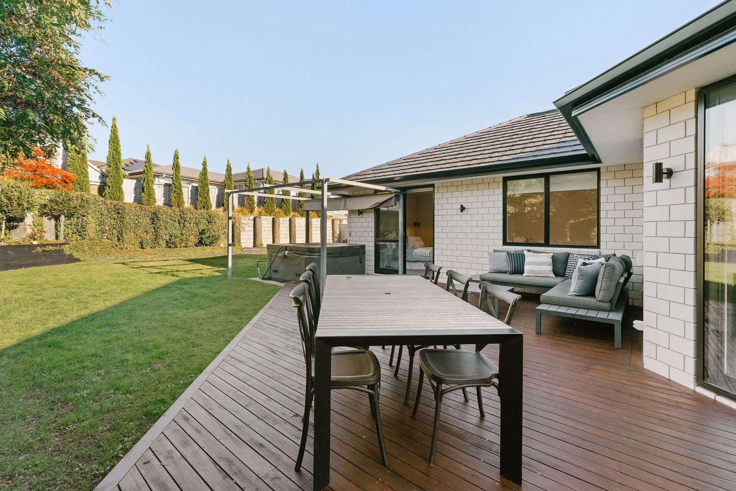 Large backyard deck with modern outdoor dining set and tall cypress trees lining the property.
