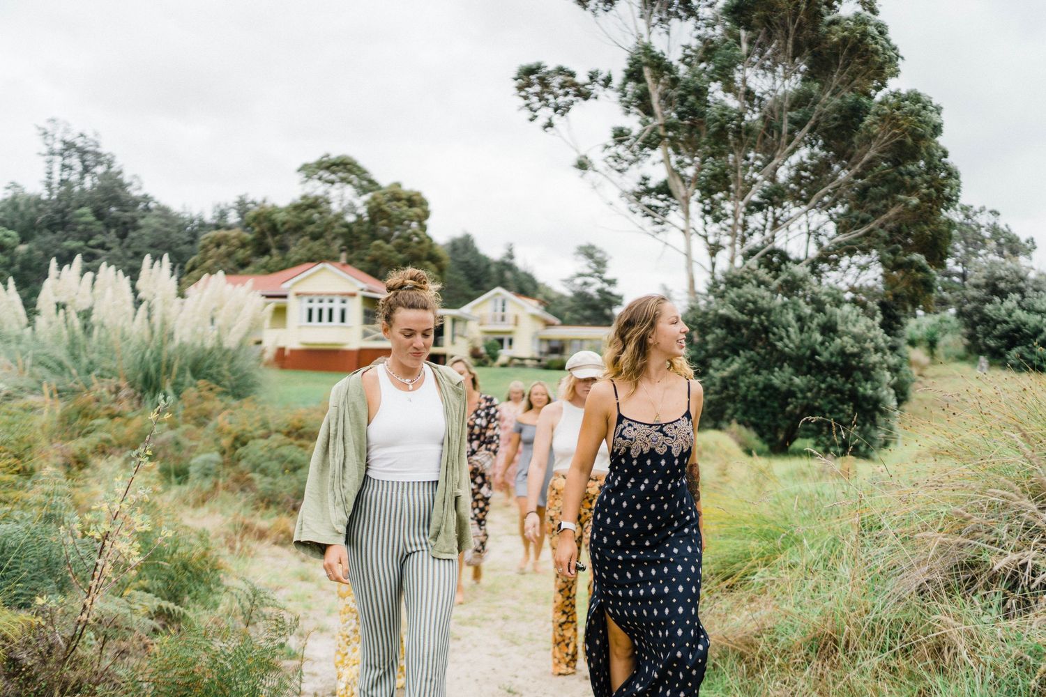 Group walking along scenic coastal path surrounded by tall grasses and trees.