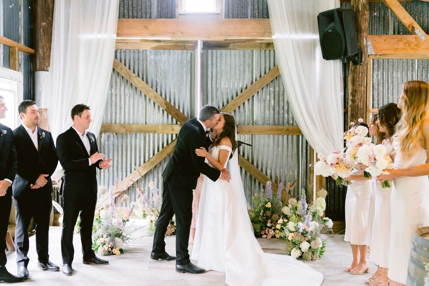 An elegant wedding ceremony setup in a rustic barn with white draping and floral arrangements.