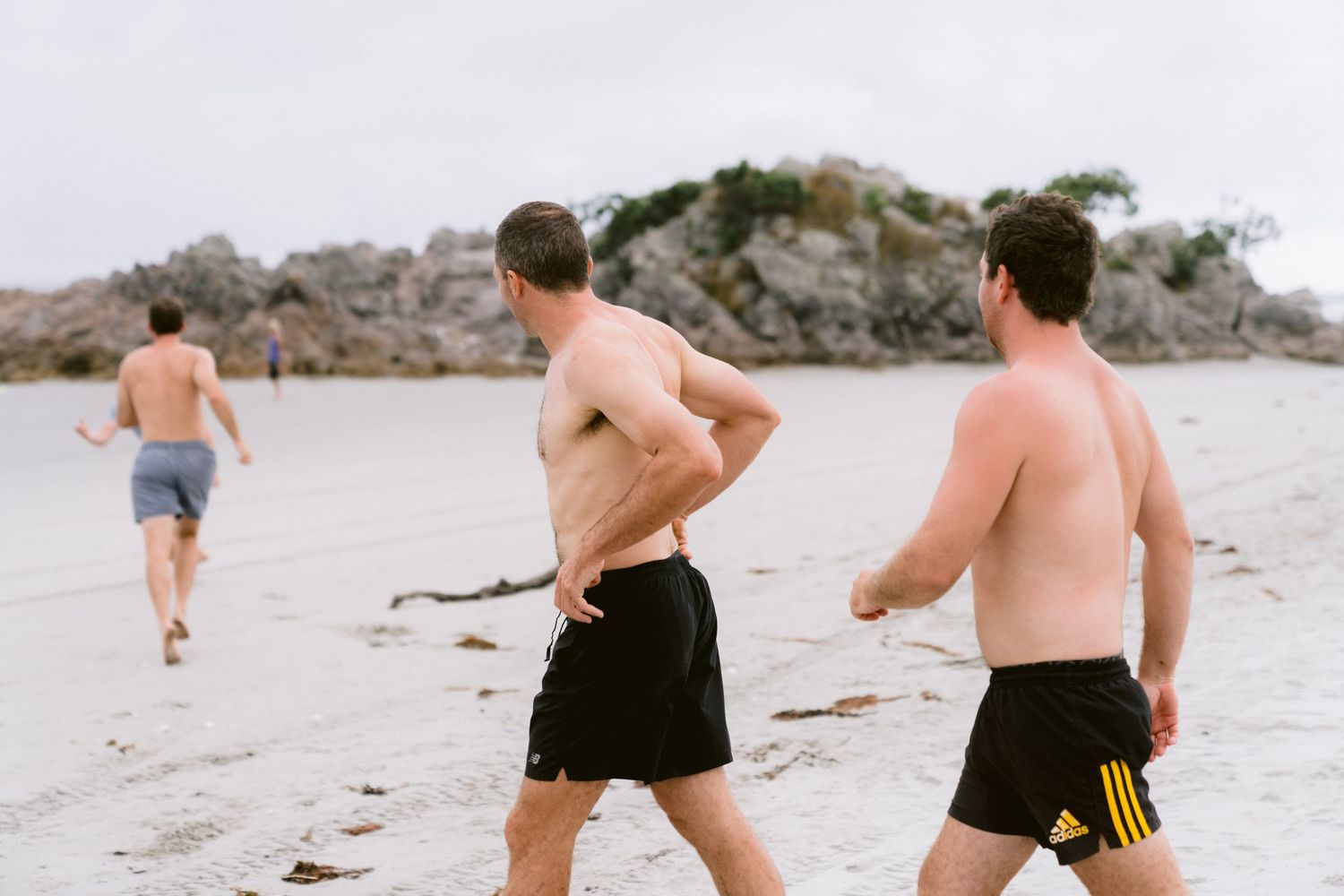 People running barefoot along a sandy beach during sunset with joyful energy and motion.