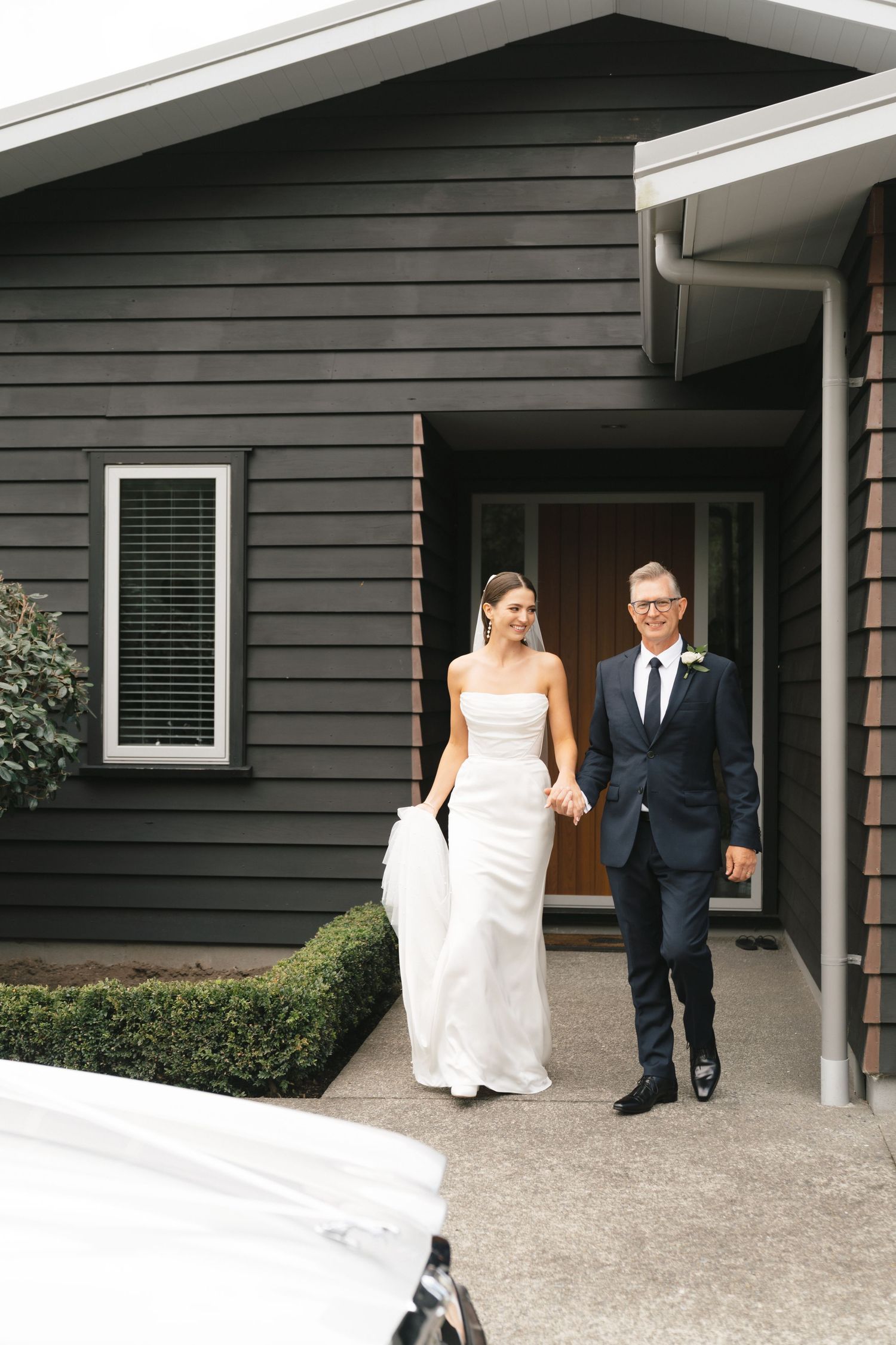 Wedding couple walking together outside modern dark grey house.