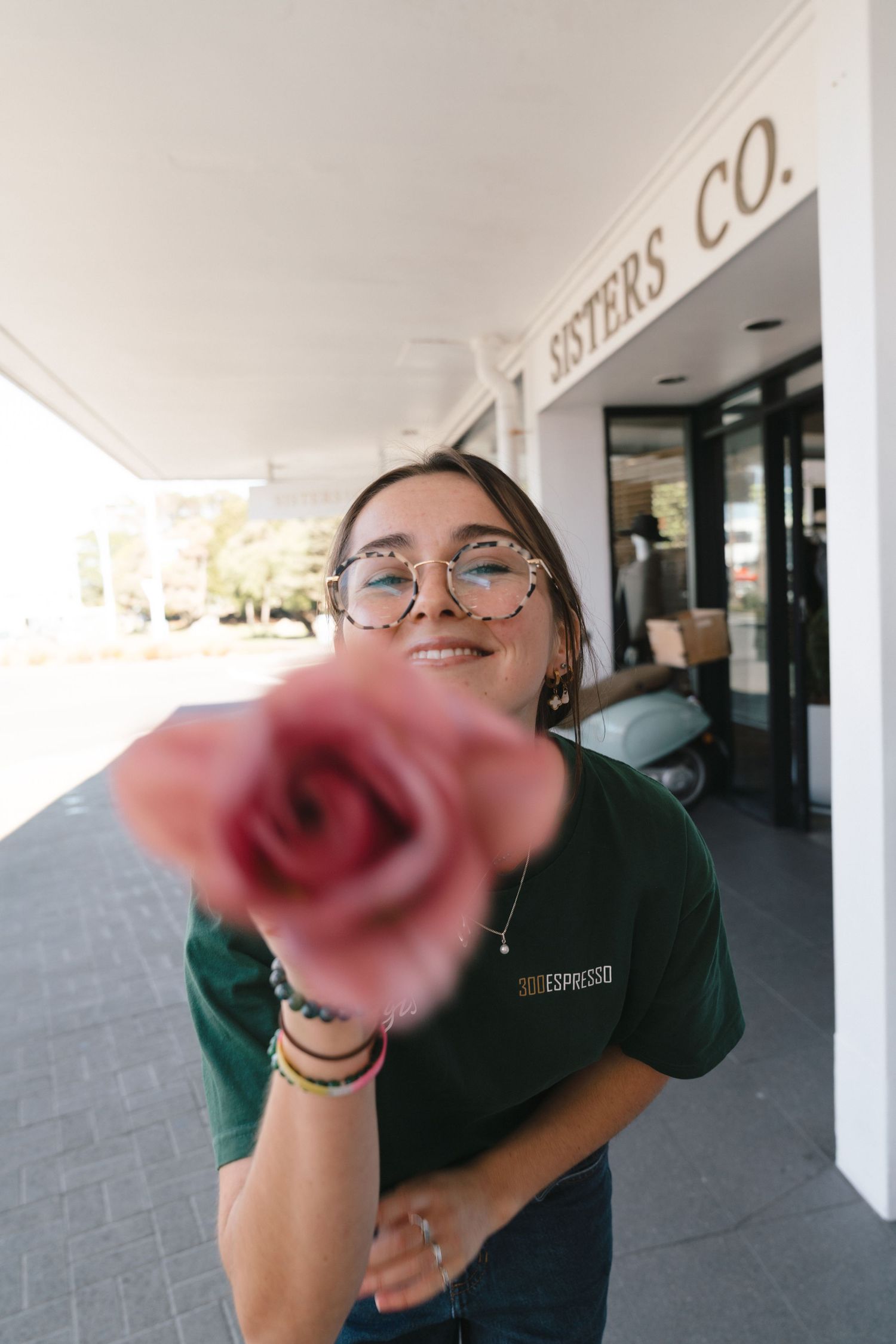 A person in glasses and dark clothing playfully poses with a pink rose in a series of three photos.
