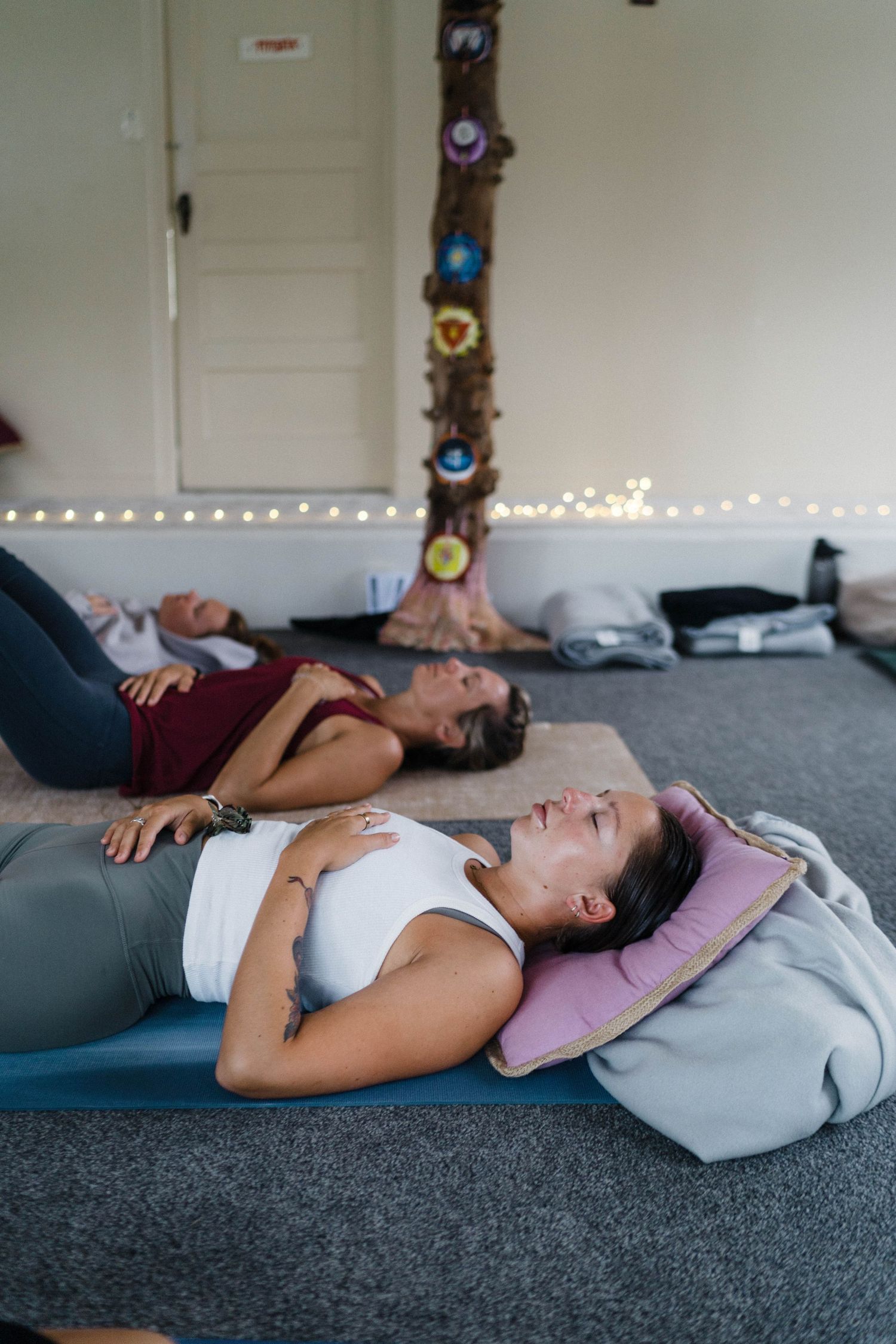 People practicing relaxation techniques on yoga mats in a cozy room with string lights.