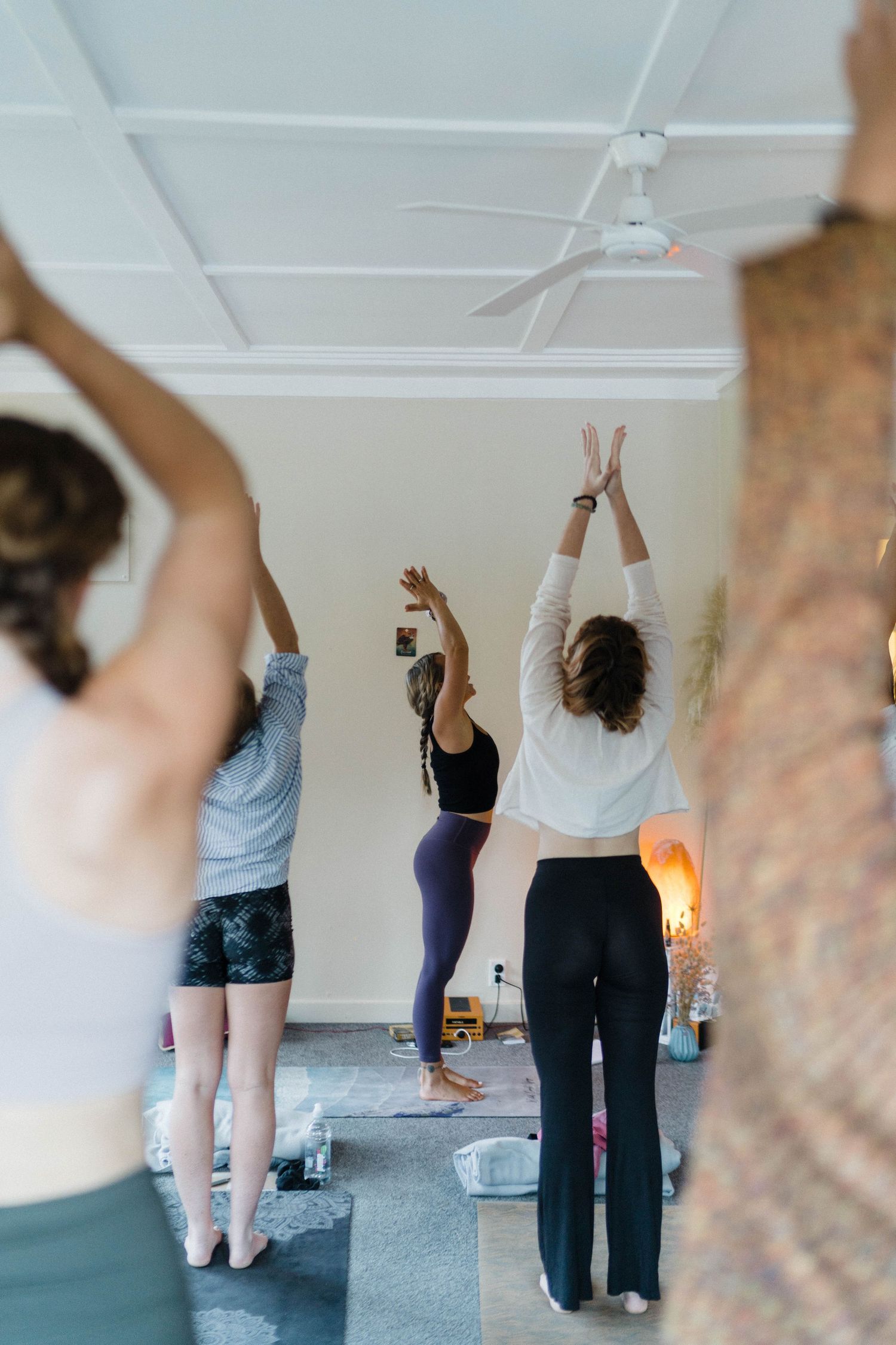 A group of people practicing yoga poses with raised arms in a bright indoor studio.