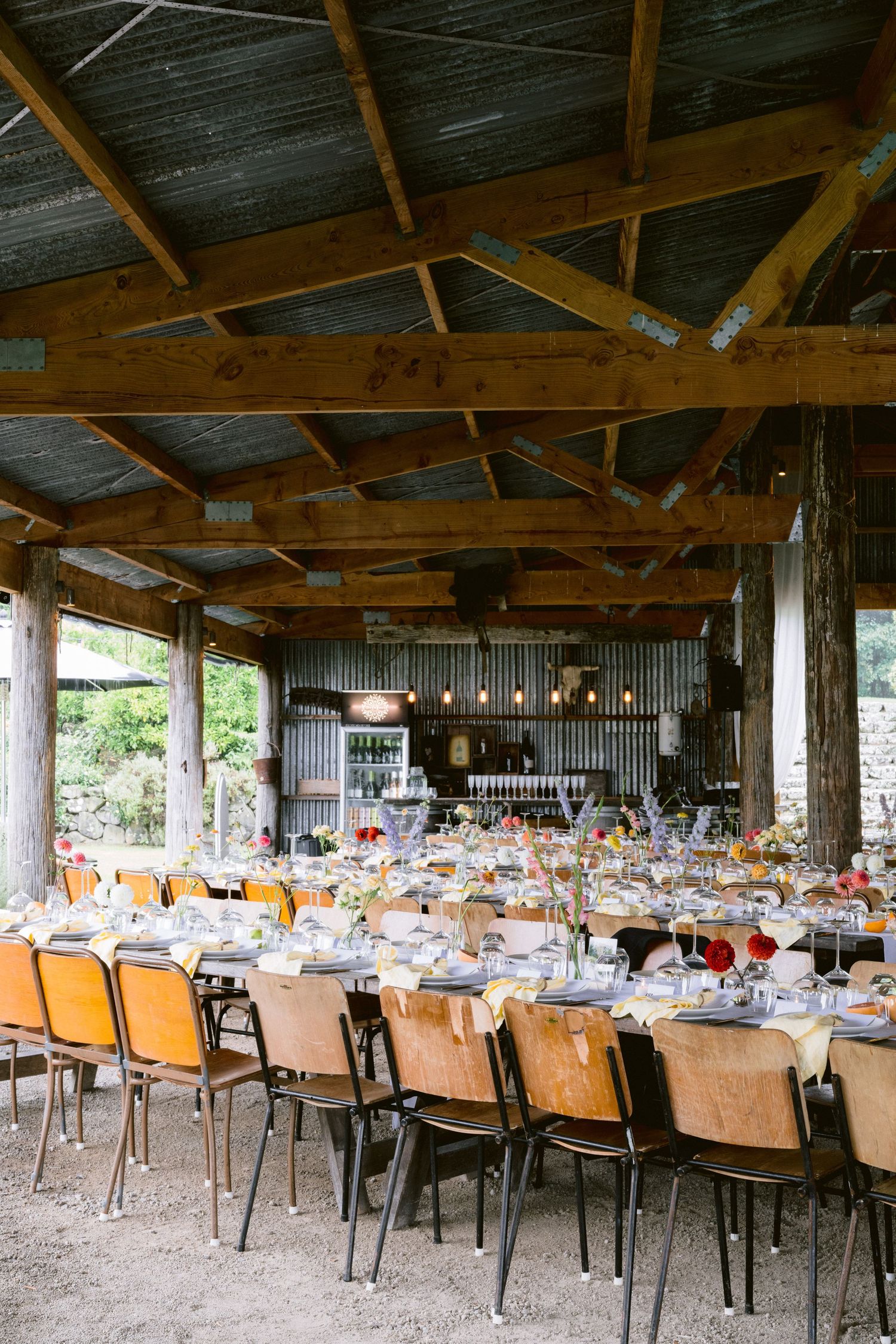 Rustic outdoor wedding reception venue with wooden beams and multiple tables set for dining.