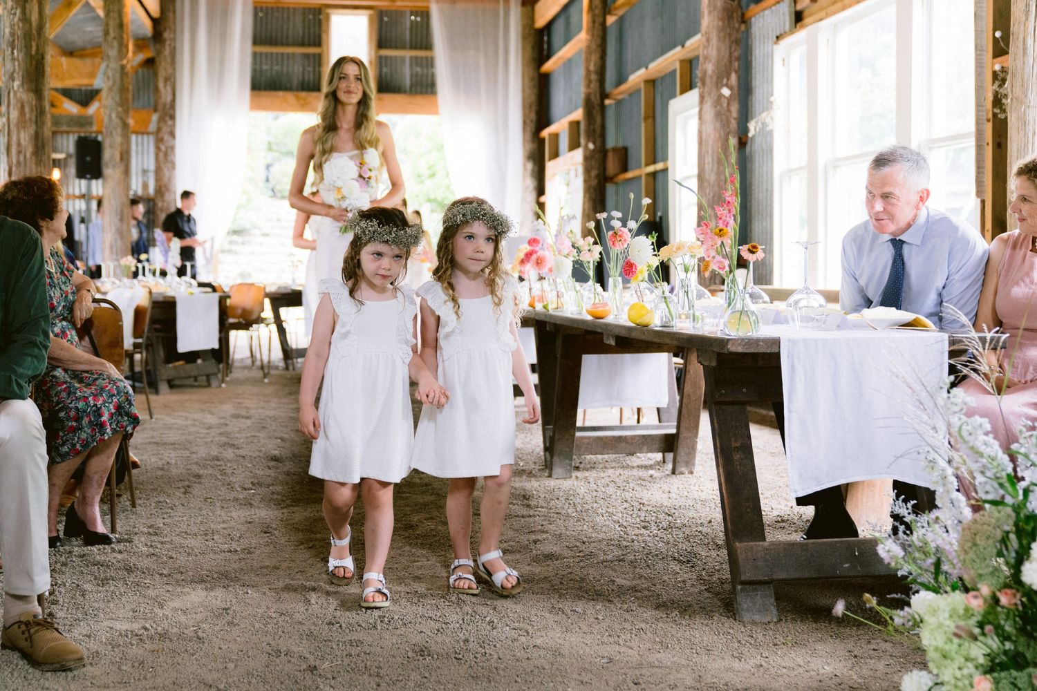 Wedding guests gathered in a rustic barn venue with natural light streaming through windows.