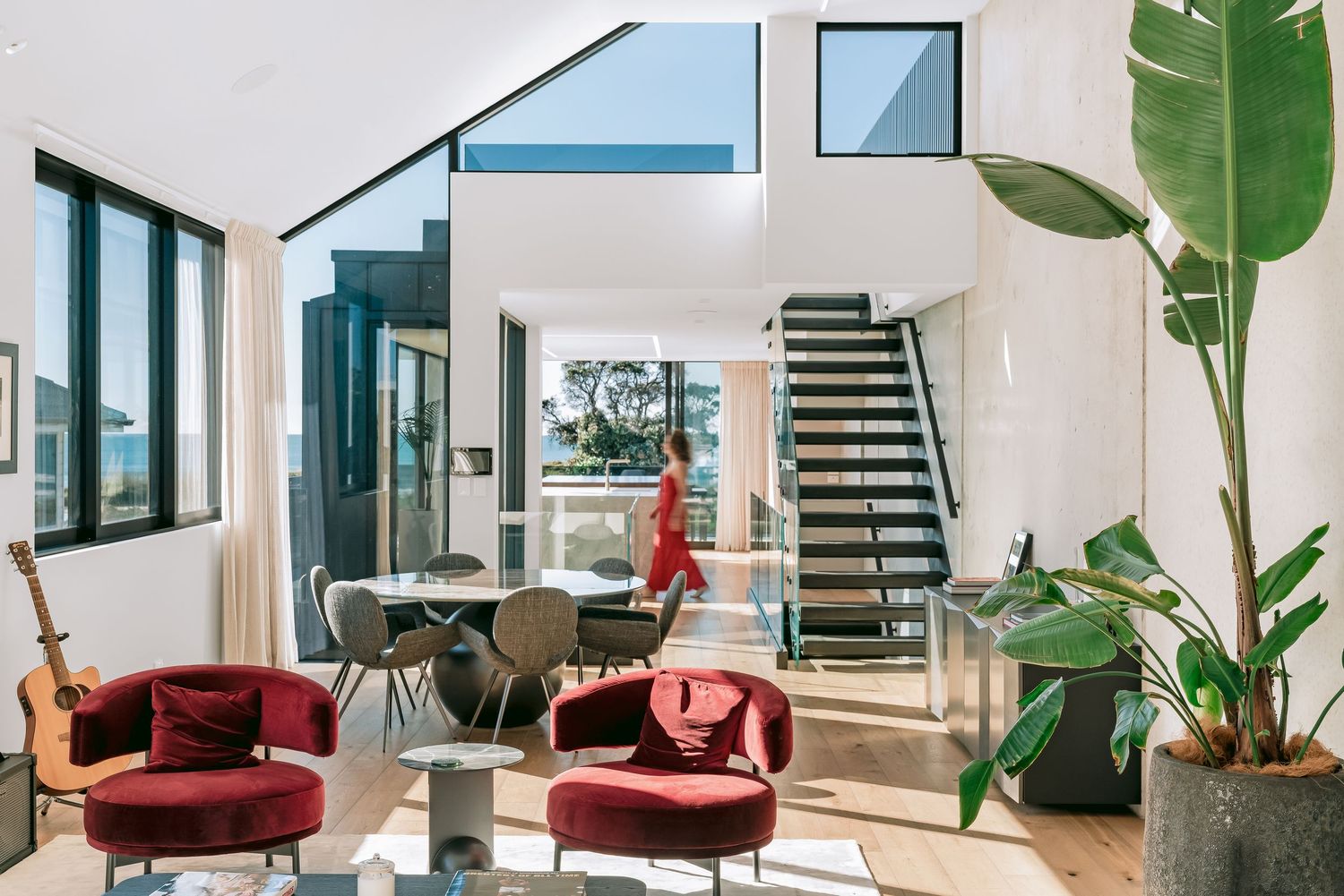 Modern living room interior with red velvet chairs, indoor plant and staircase in a bright open-concept space.